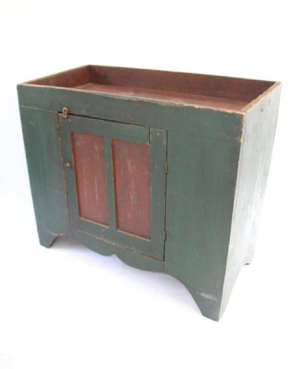 Dry sink with rectangular top with well over case with one red and green painted paneled cupboard door opening to a shelved interior on scalloped skirt with bracket feet. Retains original green and red two-tone painted surface and square nail