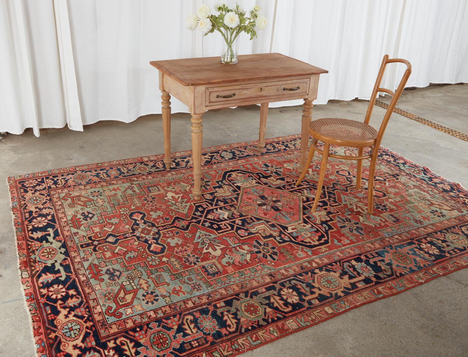 Fascinating antique 1920s Persian Heriz hand-knotted wool rug with a cotton warp. All natural dyes with vibrant colors and desirable wear featuring geometric patterns over a red field. From an estate in Beverly Hills, CA.