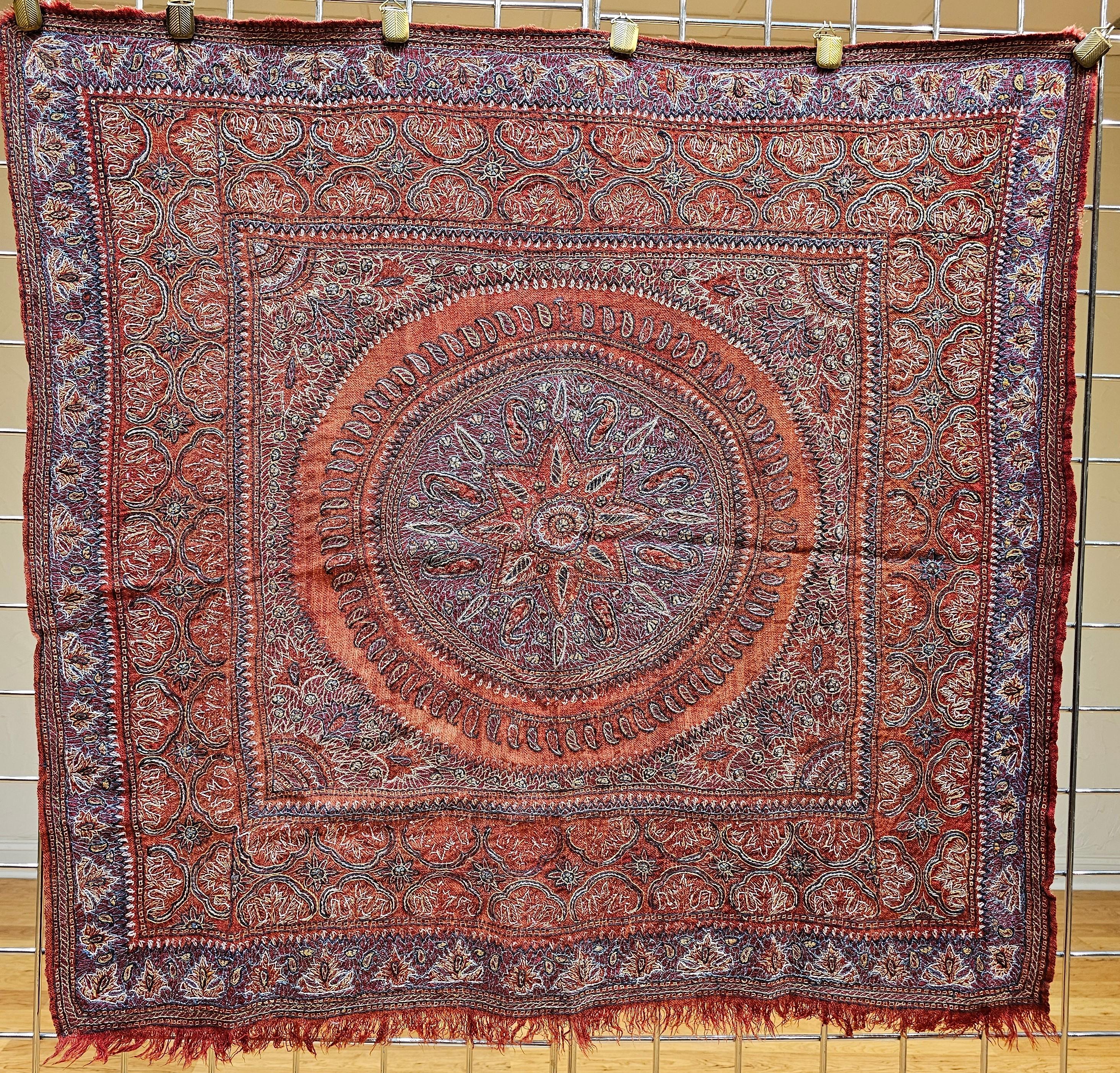 Die charakteristische persische Kerman-Suzani (Termeh-Stickerei auf Persisch) stammt aus der alten Stadt Kerman in Persien. Der handgestickte Wandteppich ist auf einem roten Stoffgrund mit Stickereimustern in Blau, Lila, Gelb und Braun. Das