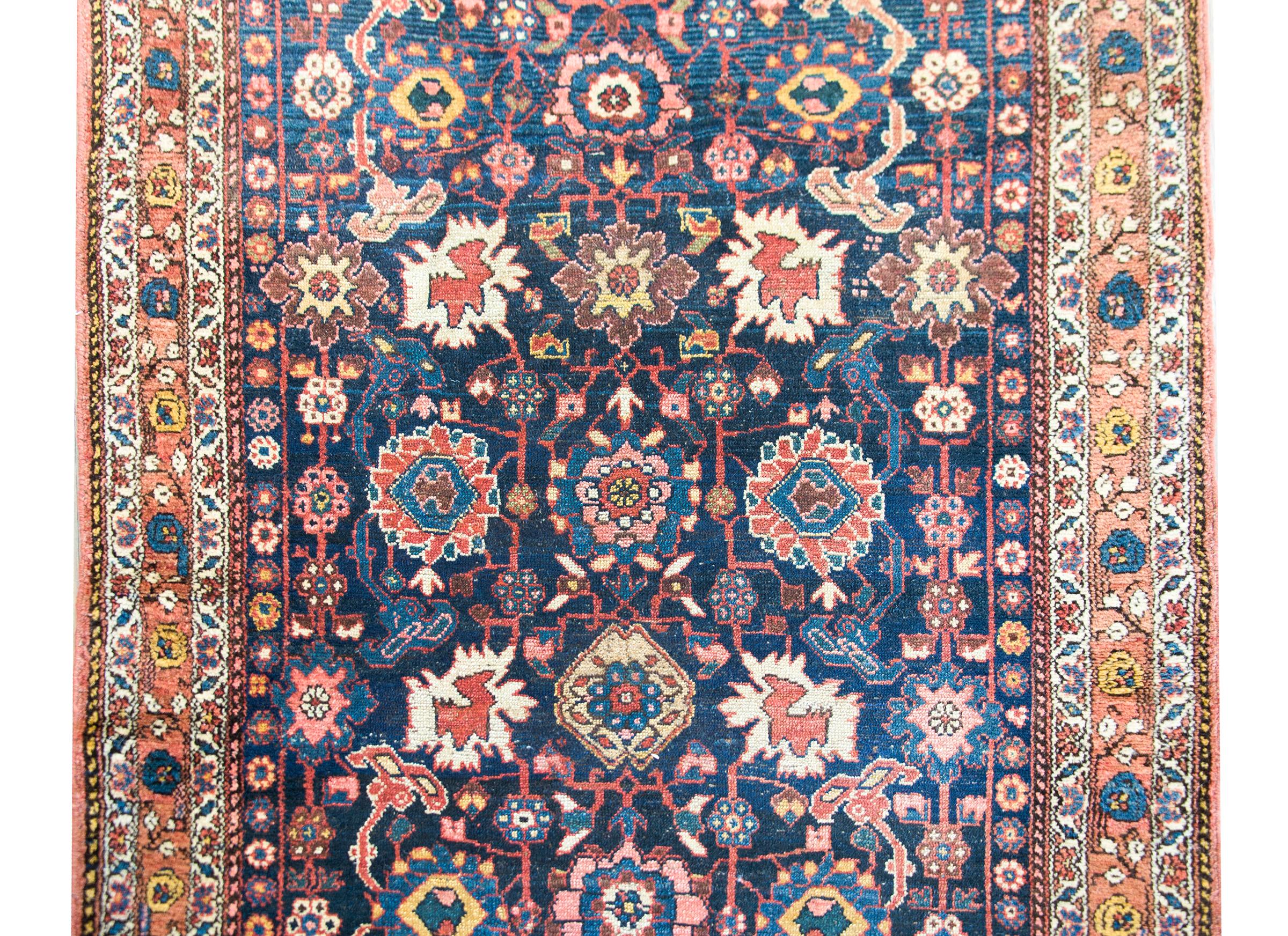 A stunning late 19th century Persian Kurdish rug with the most beautiful all-over large-scale mirrored floral pattern woven in crimson, white, gold, pink, and set against a dark indigo background. The border is equally as beautiful with a central