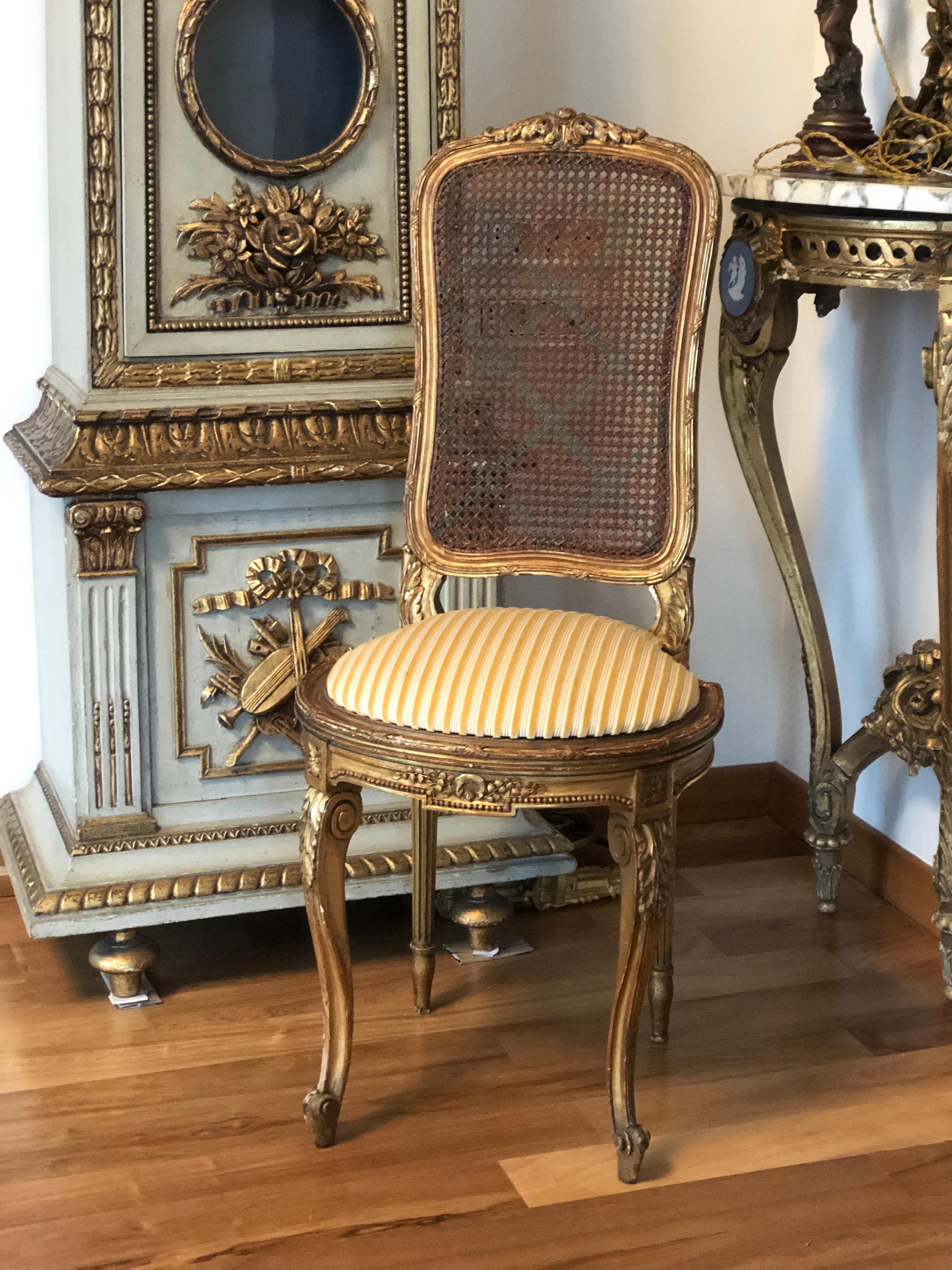 Petite chaise de salon française, de style Louis XVI, avec un cadre en bois doré et des ornements floraux sculptés. Les pieds avant sont incurvés et l'assise est semi-ronde à l'avant, avec un coussin à rayures en velours moutarde. Le dossier et