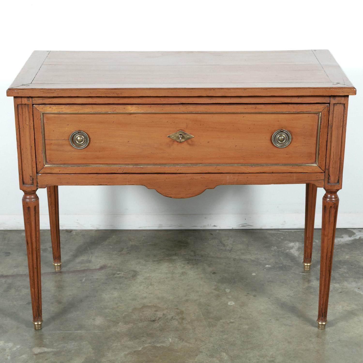 A 19th century petite French Louis XVI commode handcrafted of solid cherry with a wonderful warm patina, circa 1890s. Having a rectangular top, this handsome one drawer commode features brass trim and original brass hardware. Carved apron resting on