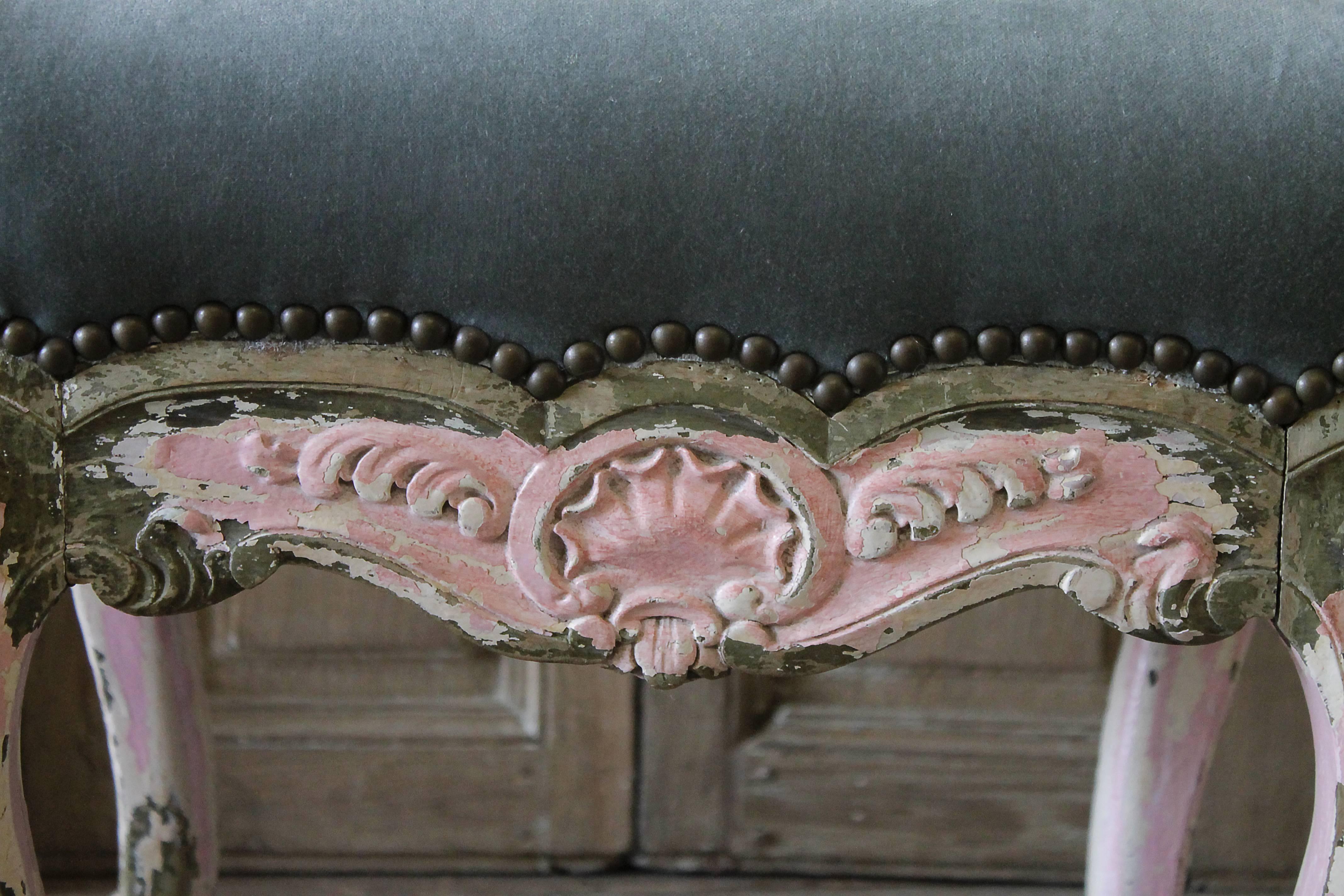 19th century Petite French painted Louis XV style vanity stool
with original chippy paint in a soft pink, cream exposing original natural wood tones underneath.
Upholstered in a blue velvet with antique aged brass colored nail trim.
Legs are very
