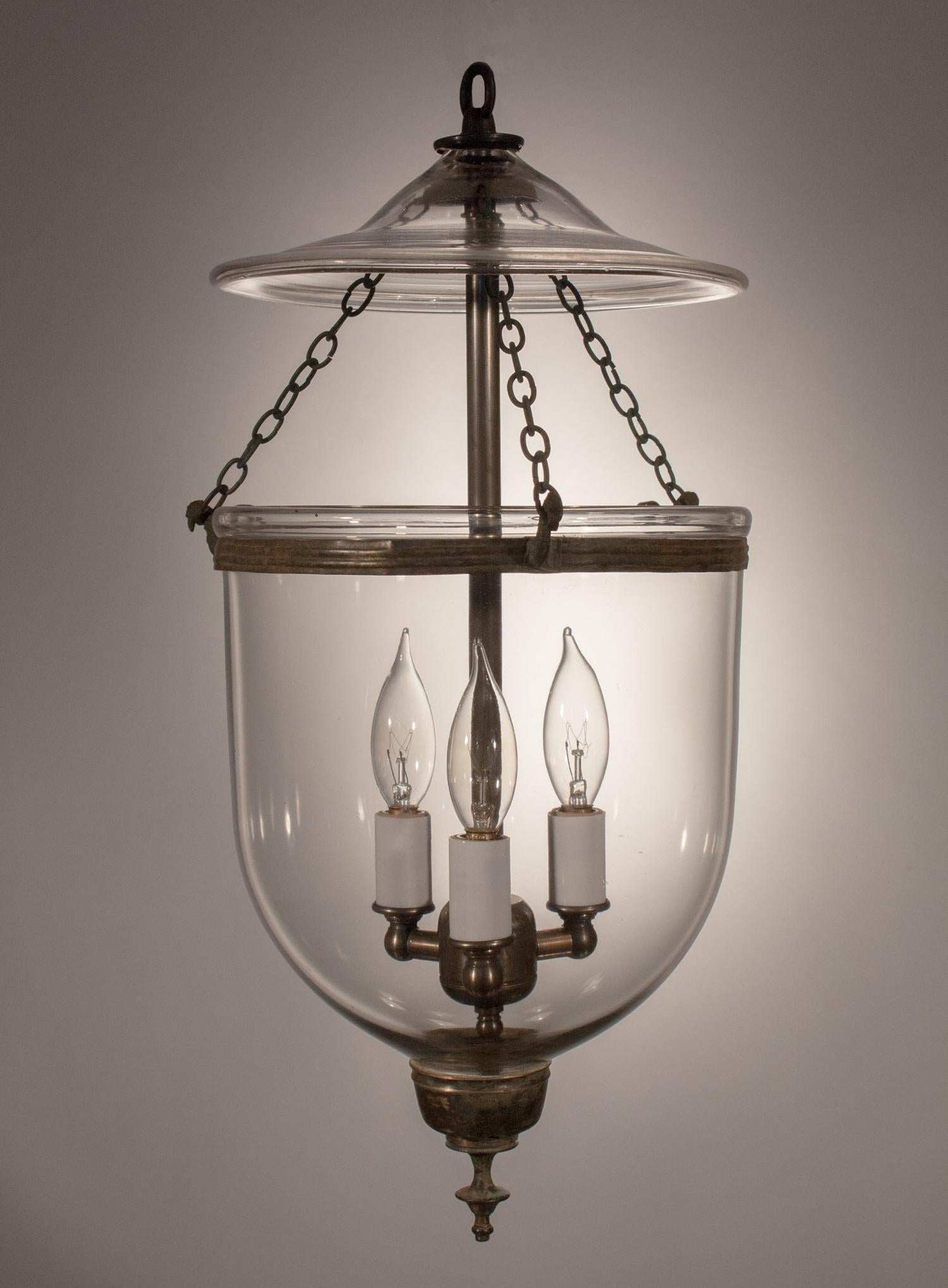 A lovely bell jar lantern with its original chain, rolled brass band and finial candleholder base. This petite hall lantern features excellent quality handblown glass. It has been newly electrified with a three-bulb candelabra cluster accommodating