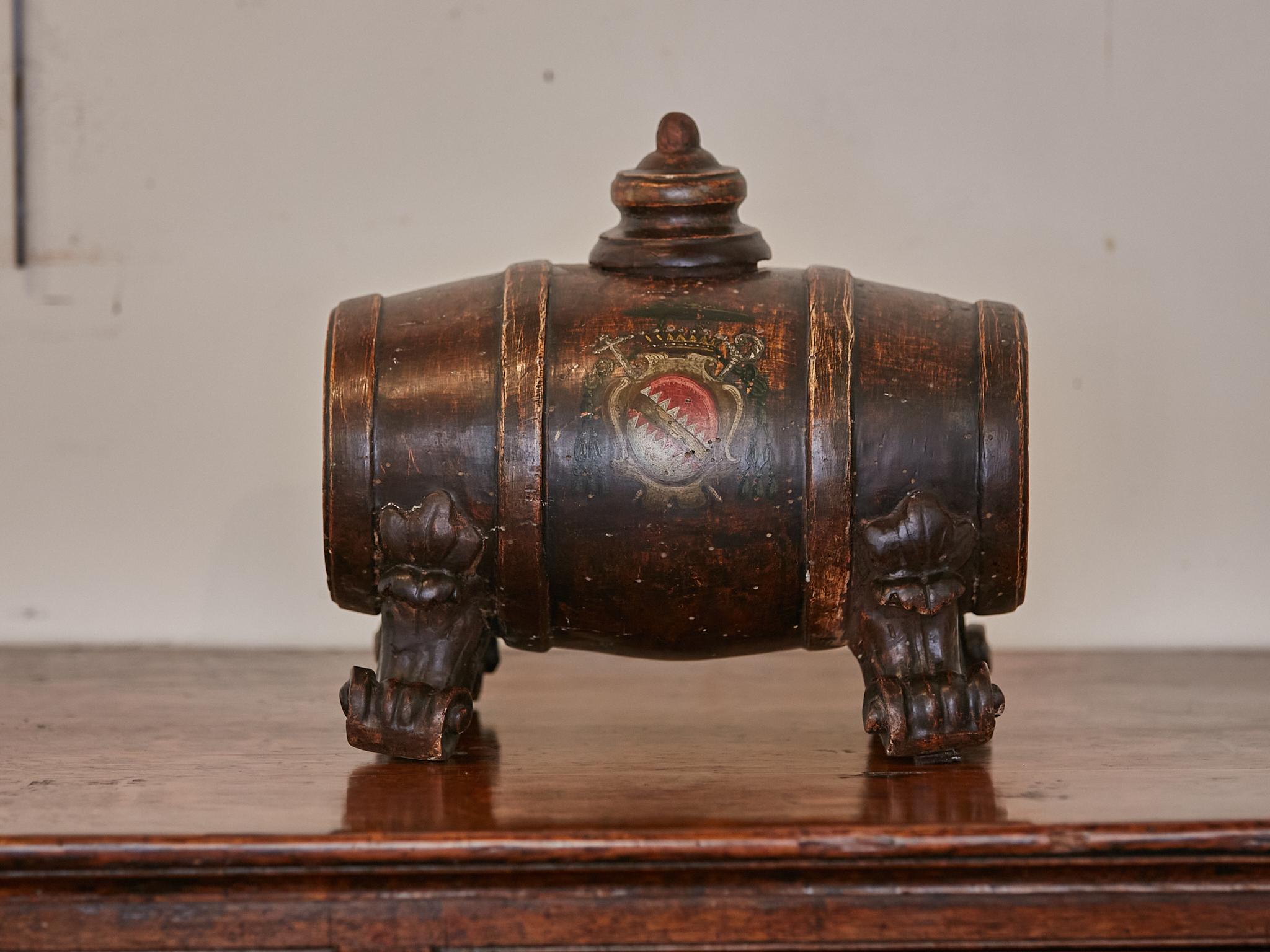 A small Italian wooden spirit barrel from the 19th century (or earlier) with carved scrolling feet, painted heralding shield on the belly and nice patina. Immerse yourself in the rich history of Italy with this wooden spirit barrel, a cherished