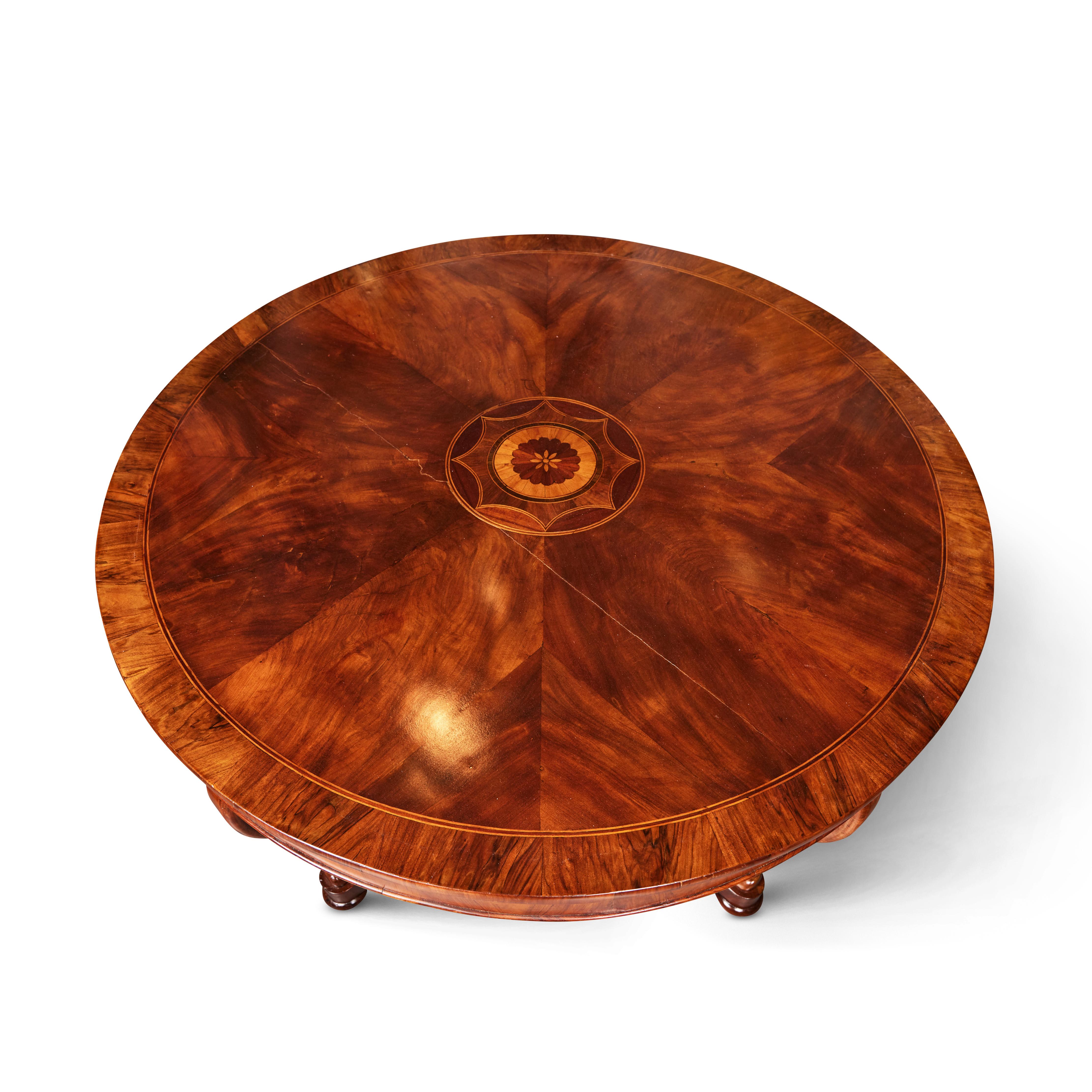 A large scale, hand-carved, veneered and inlaid, walnut and fruitwood center table with a book matched top centered on a  radiant medallion. The base featuring a central, turned column surrounded by four, unusual, two-tier, convex-concave scrolling