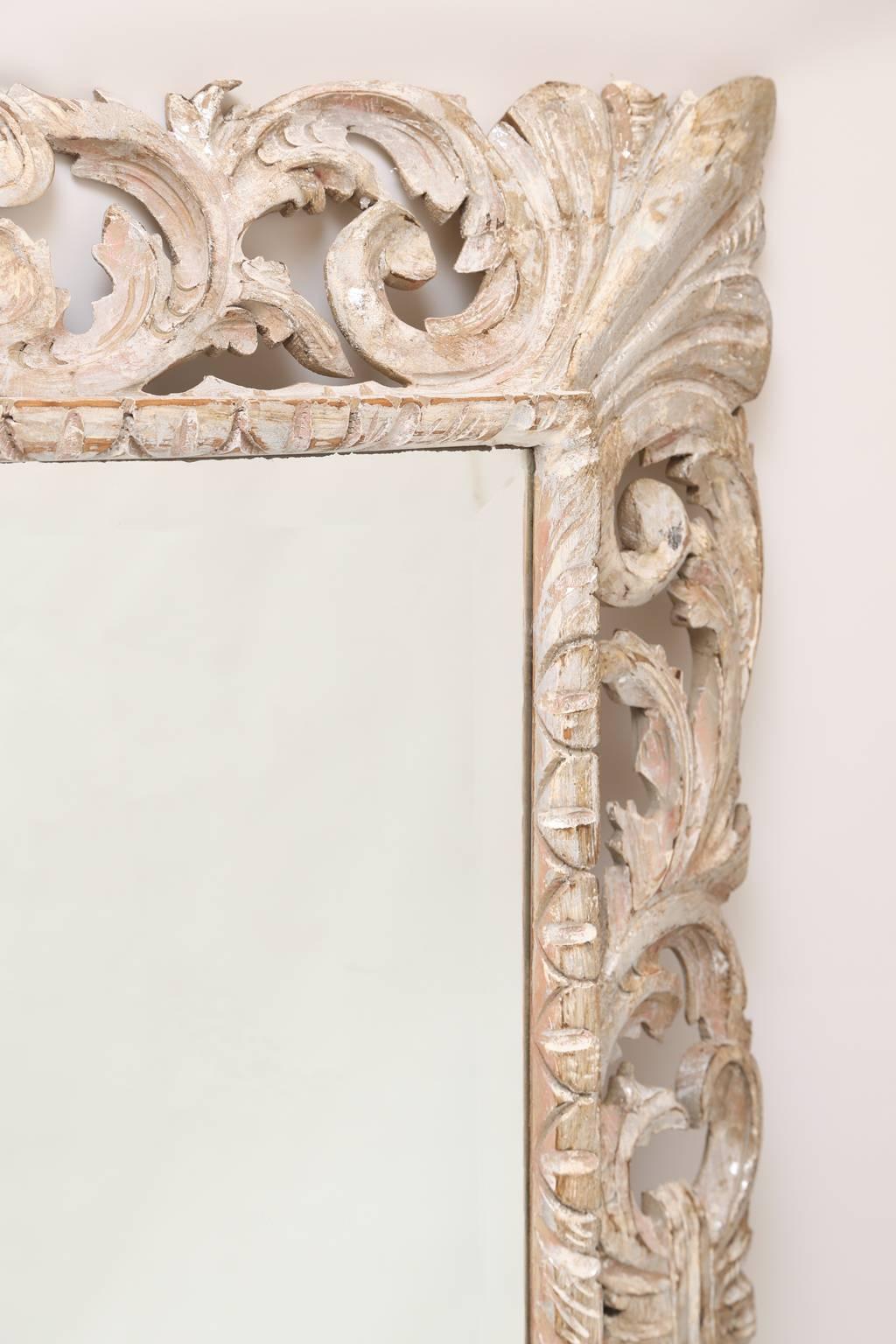 Miroir mural, en bois sculpté à la main, finition bois naturel et décapé, avec une parcelle de dorure argentée, présentant une plaque de miroir biseautée, montée à l'intérieur d'un cadre rectangulaire, décoré de godrons, bordé de feuilles d'acanthe