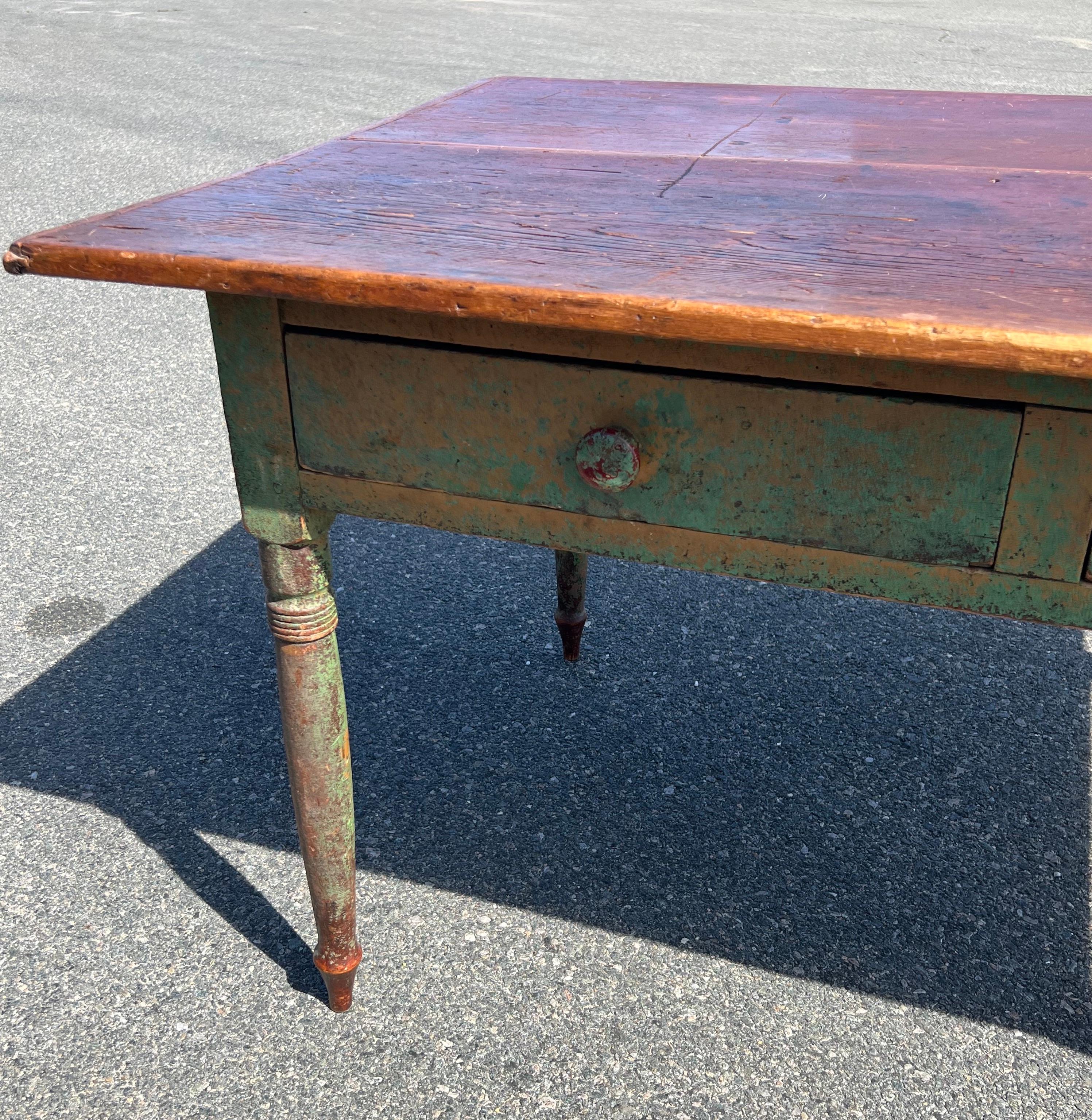 19th Century Pine Desk Table.  Unpainted two board top with thin breadboard ends.  Base in old green and yellow paint over original red paint.  Two drawers, side-by-side, and turned legs.  Overall pegged construction.