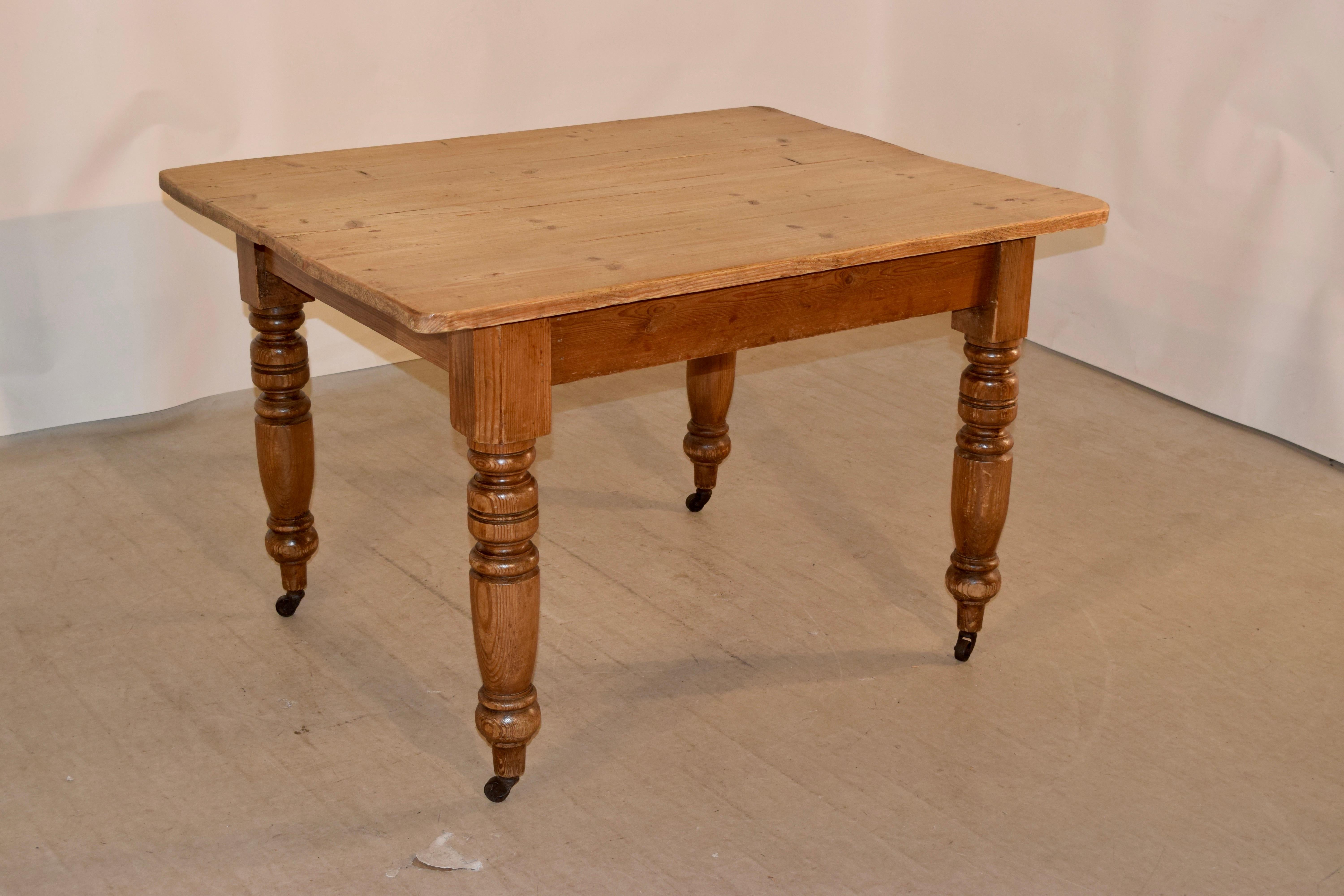 19th century English pine farm table with a four plank top, following down to simple aprons and supported on thickly hand-turned legs, supported on what appear to be original casters. The apron measures 24 inches in height.