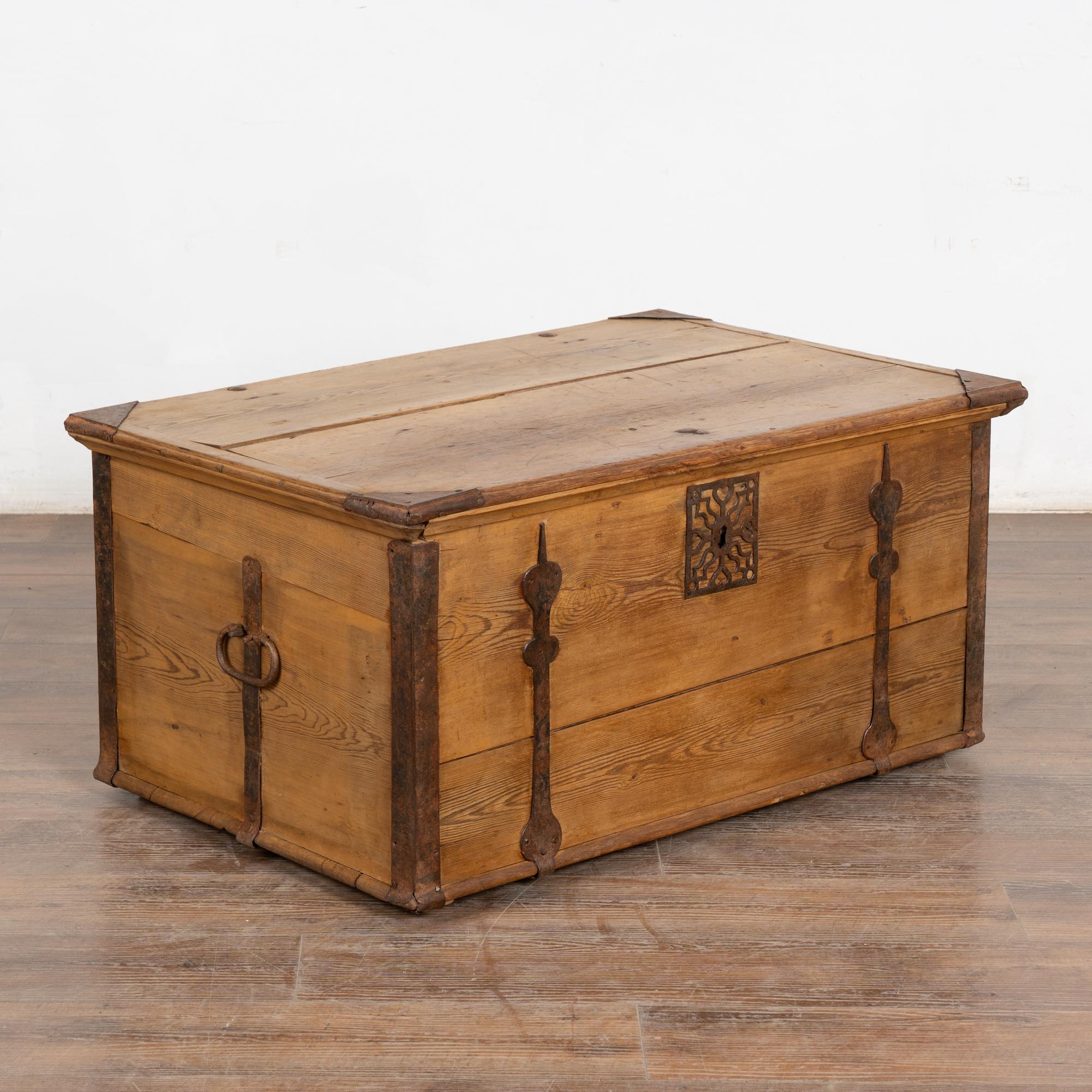 The pine in this flat top trunk has grown warm with a patina that comes only from the passage of years and use. 
Note the hand-wrought iron corners, long straps/hinges, side handles, and decorative element around key hole. 
Restored, waxed, strong