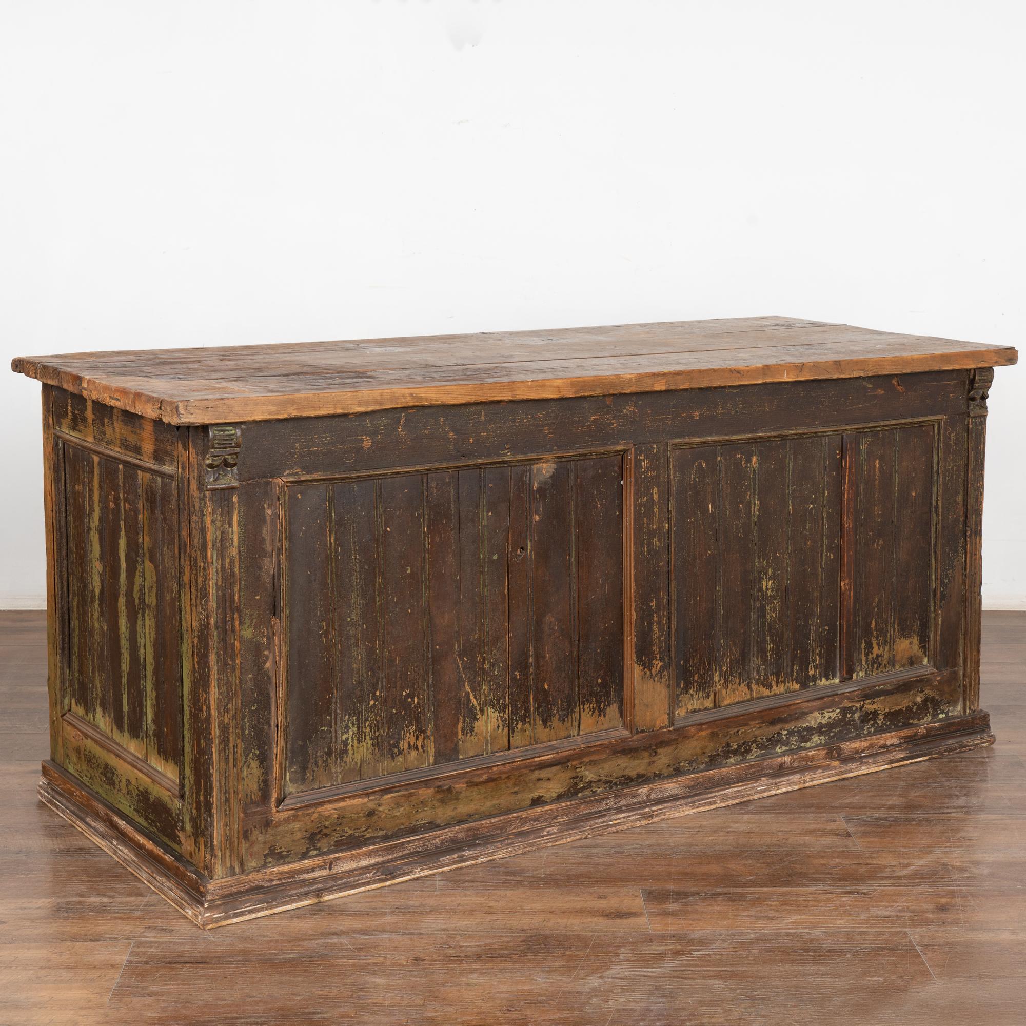 Antique free-standing shop counter with brown painted finish, 6' long.
The old brown paint is distressed throughout adding to the authentic vintage feel of this sideboard; touches of green underneath.
The top is natural pine with scratches, cracks,