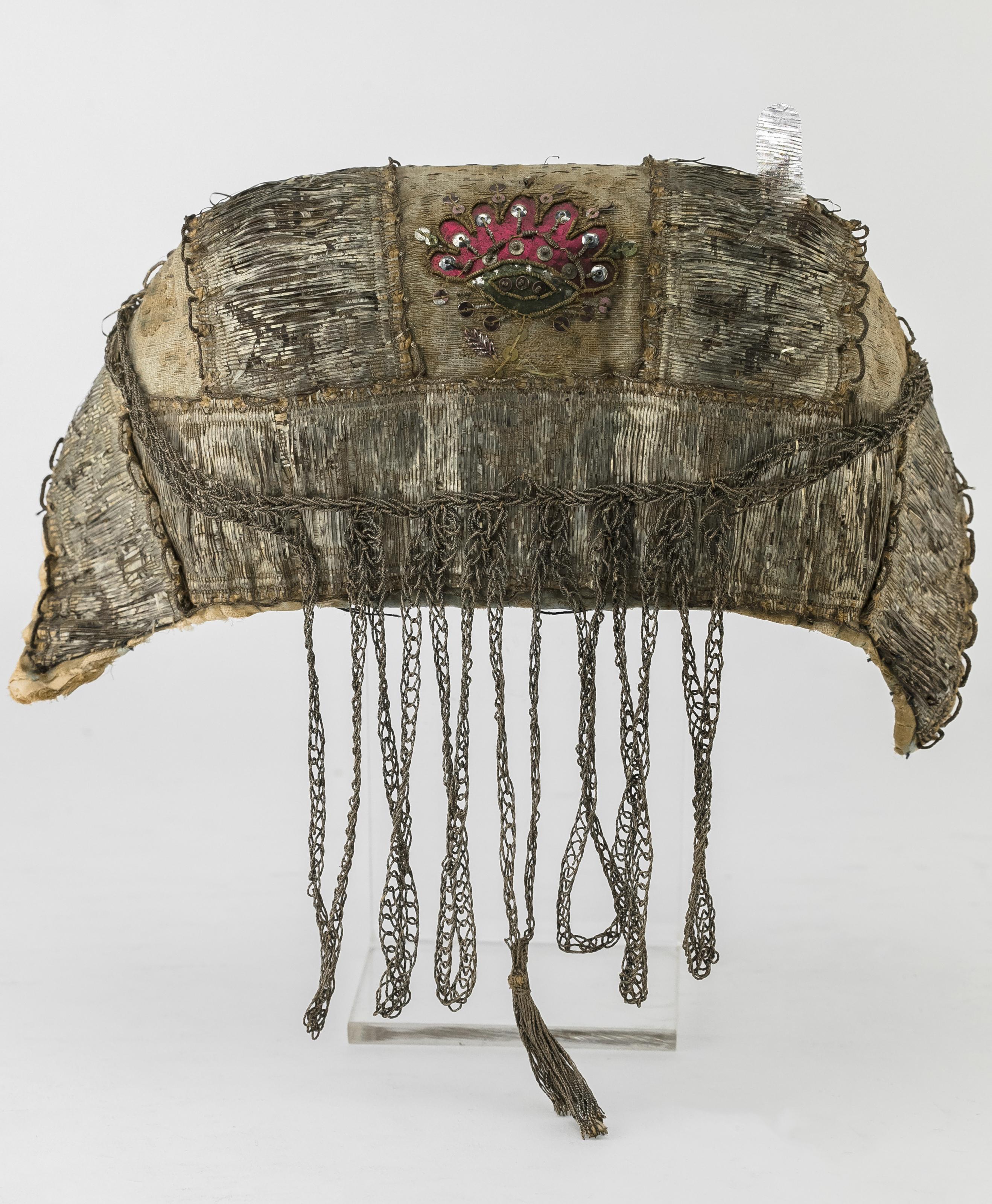 Gold and silver wrapped thread on canvas, gold thread embroidery, embellished with decorative appliques and sequins; silk lining.
Rare example of a magnificent cap worn on the Sabbath and holidays to cover the hair of a well-to-do married Jewish