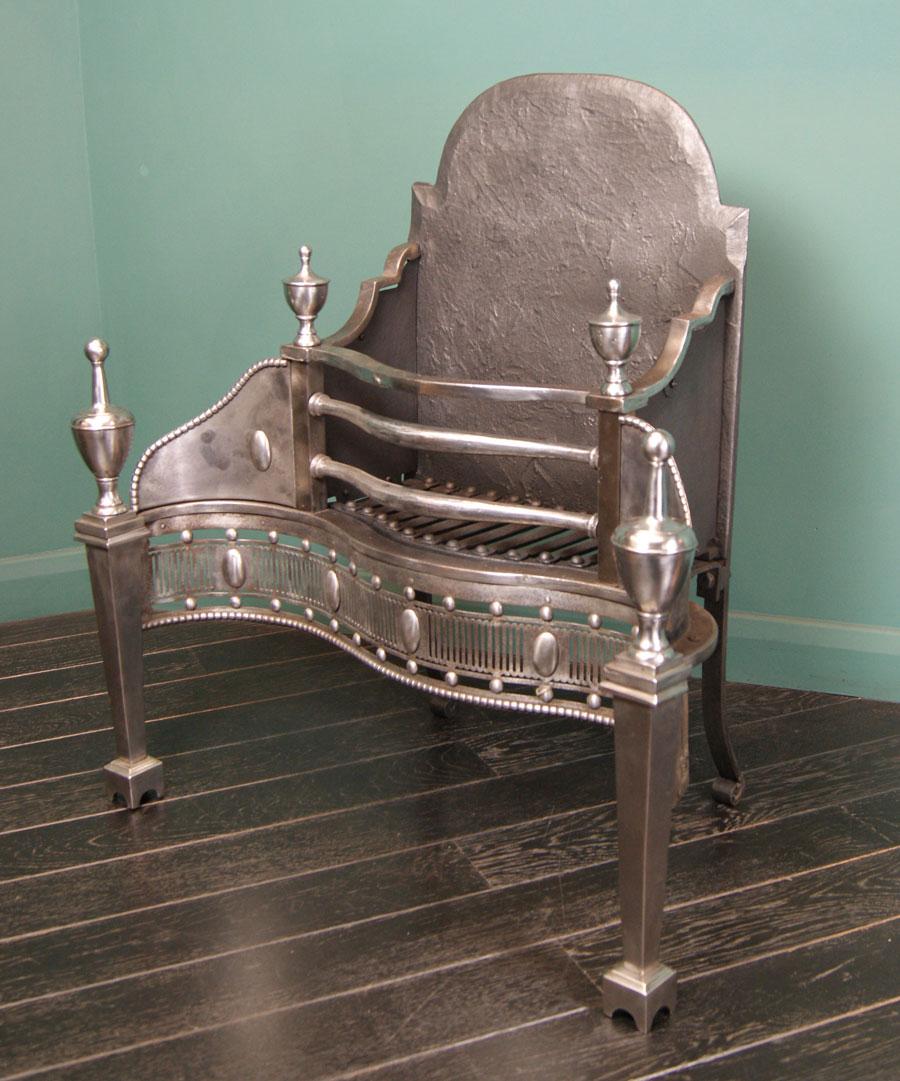 An elegant, tall 19th century polished steel dog grate. Tapered legs set on arched plinths under pinnacle urn finials. Serpentine front with pierced fluted fret plate interrupted with paterae over beaded moulding. Rear elements consist of rivet-work