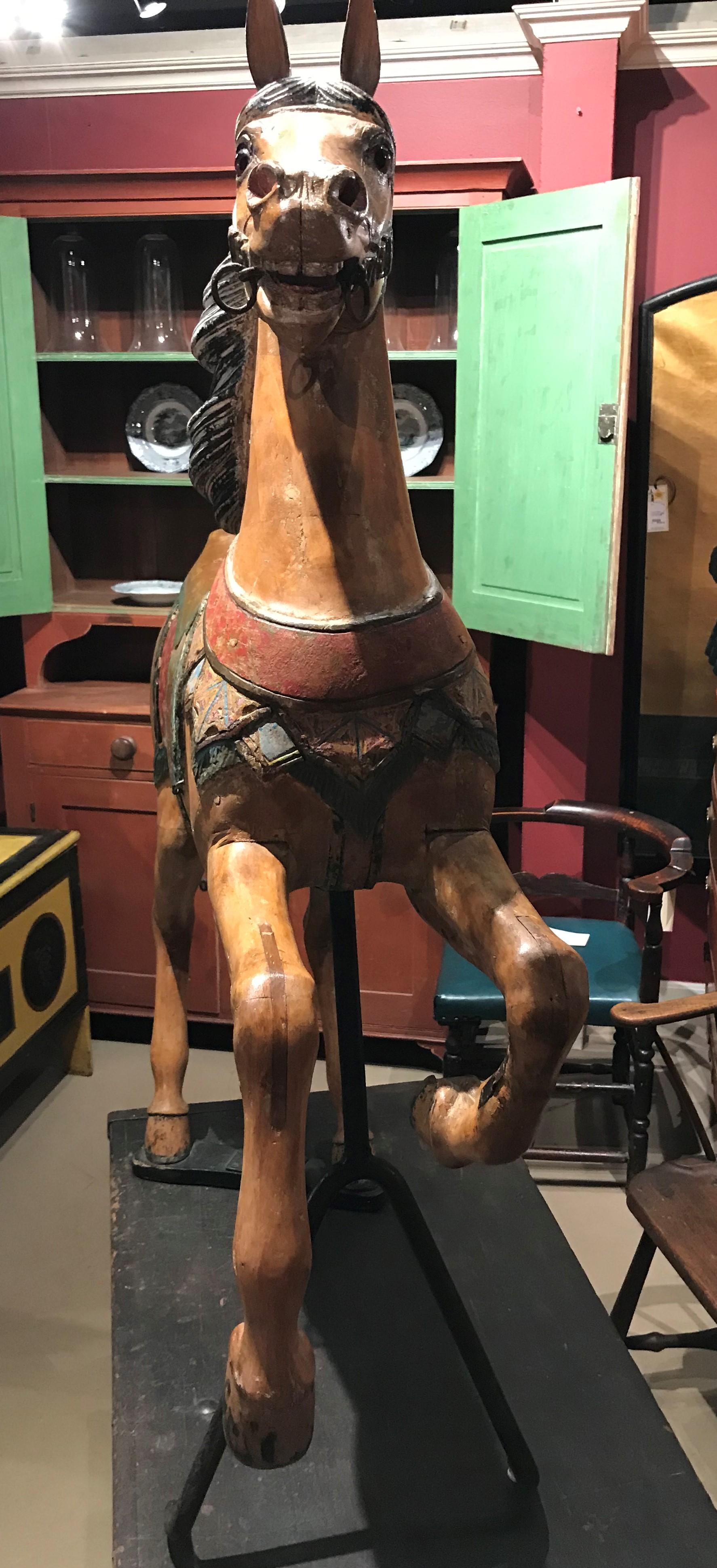 A fine carved and polychrome wood prancing carousel horse with saddle and horse-hair tail. Removable iron fork stand. Rear legs attached to a single plank. Good overall condition, with some paint loss, one front leg with repair, other small
