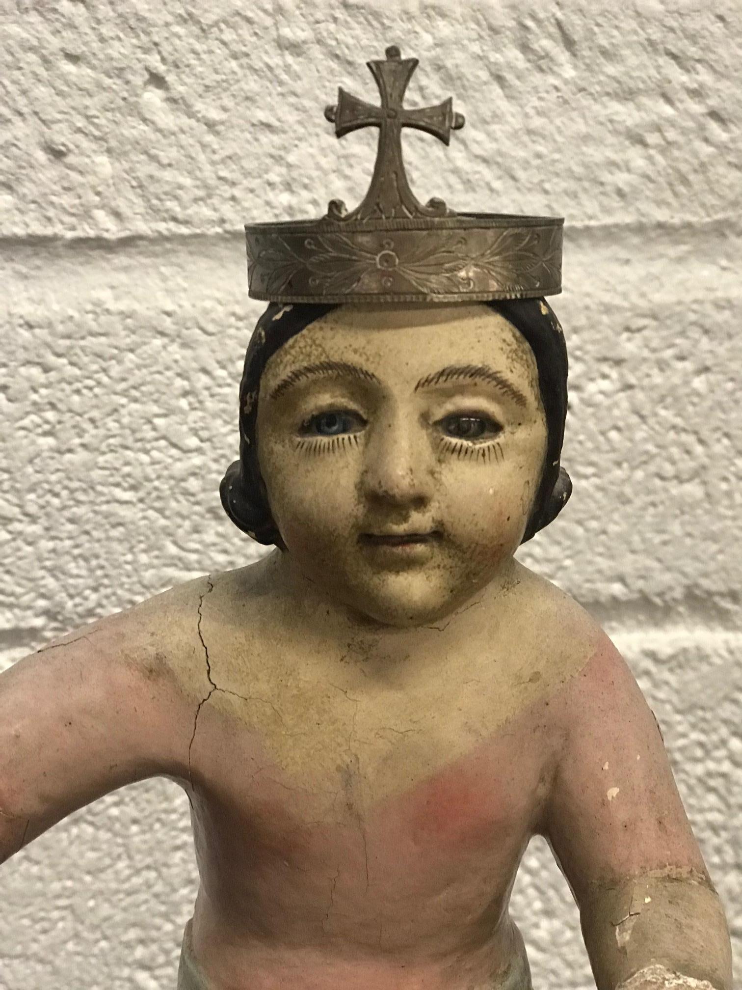 Beautifully carved and sculptured polychrome nino. Glass eyes. Has a metal crown that sits on his head but is not the original. We believe that he held a staff in one hand and a globe in the other. Some missing fingers. He shows signs of his age,