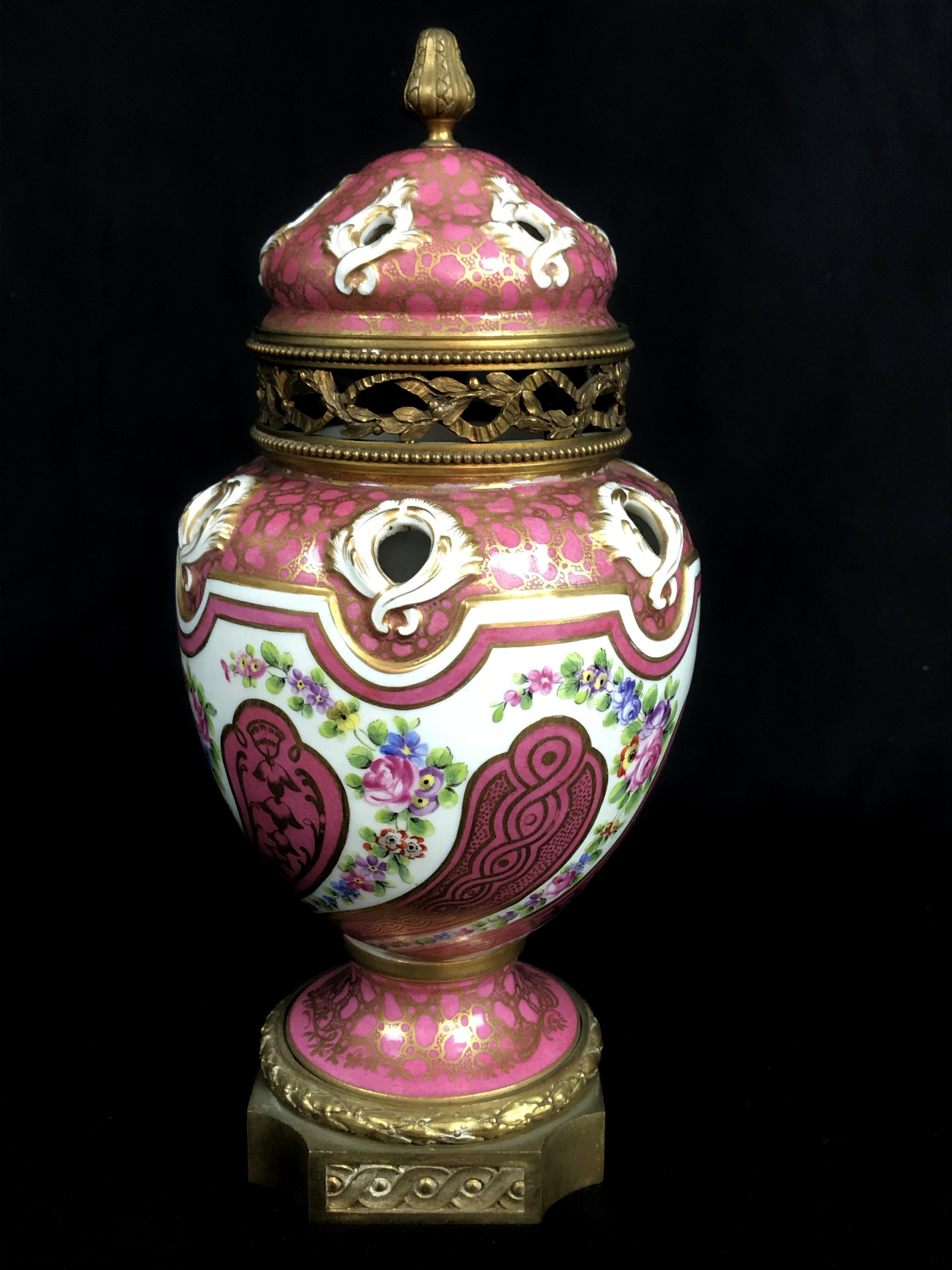 Refined polychrome porcelain perfume burner, in the shape of potiche, painted with refined geometric decorations in gold on a light magenta red background and splendid bouquet of flowers. The base and the band of the perforated lid, with foliate