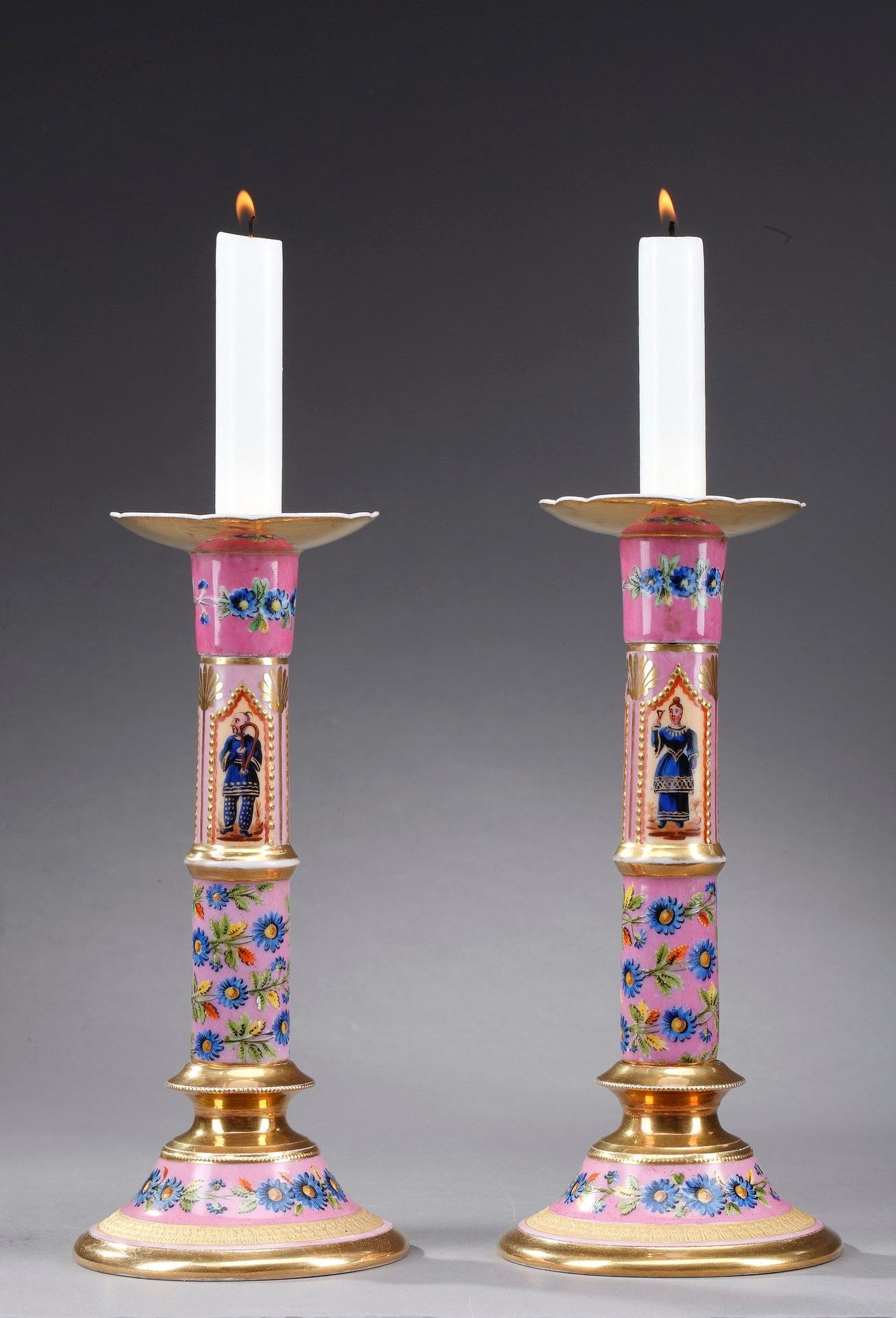 This enchanting pair of Restauration candlesticks is crafted of Paris hard-paste porcelain. Both lights exhibit multicolored decoration including oriental characters and a multitude of flowers on pink background. Each torch rests on a round foot