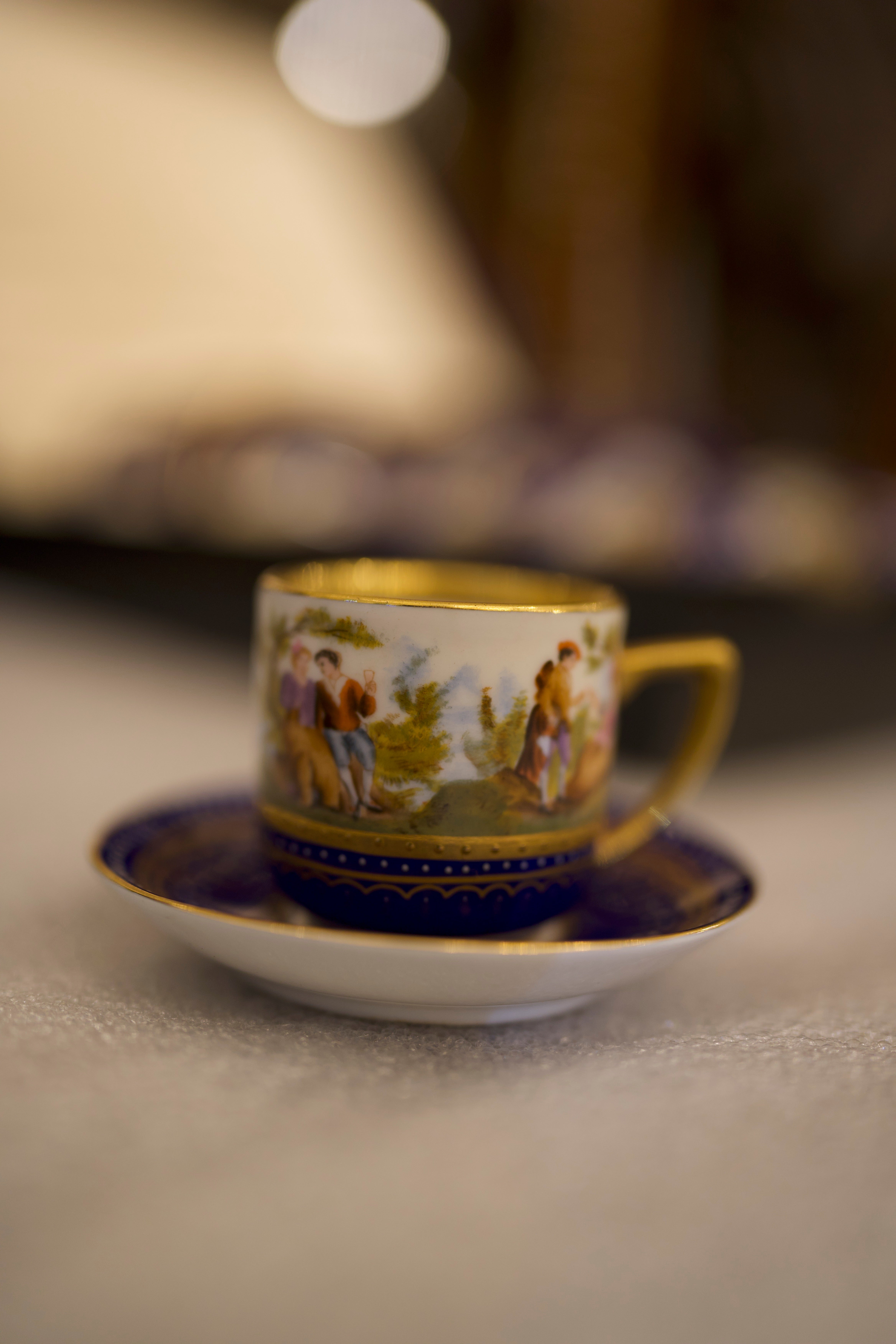 19th century Elegant 12 Piece painted, cobalt blue porcelain cups and saucers, with a genre, Neapolitan scene; cylindrical shape, with a rectangular handle. Decorated with gold.