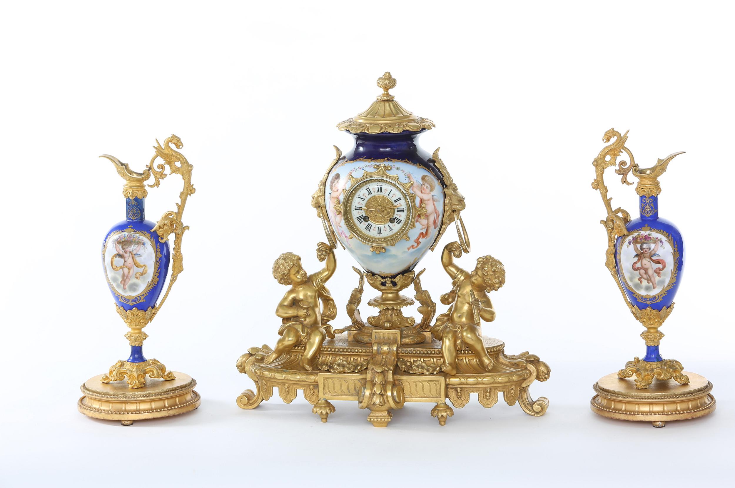 19th century Regency revival porcelain with gilt bronze mantel clock on stand with a pair of neoclassical revival ormolu mounted one handled amphora shaped ewers. The pieces are in great antique condition. Minor wear consistent with age / use. The