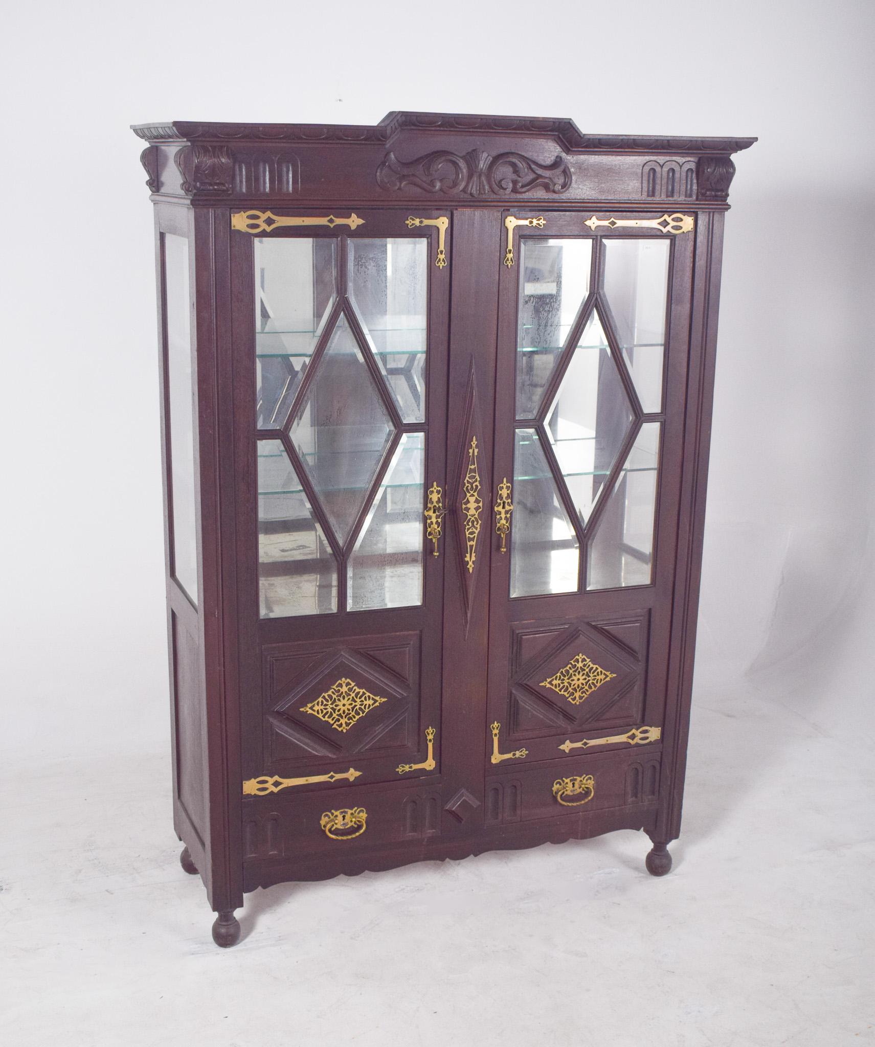 Dutch-style china cabinet with brass fittings. In dark wood with rich and striking decoration, of obvious Dutch inspiration, possibly dating from the late 19th or early 20th century. The structure features two glazed doors with faceted glass in a
