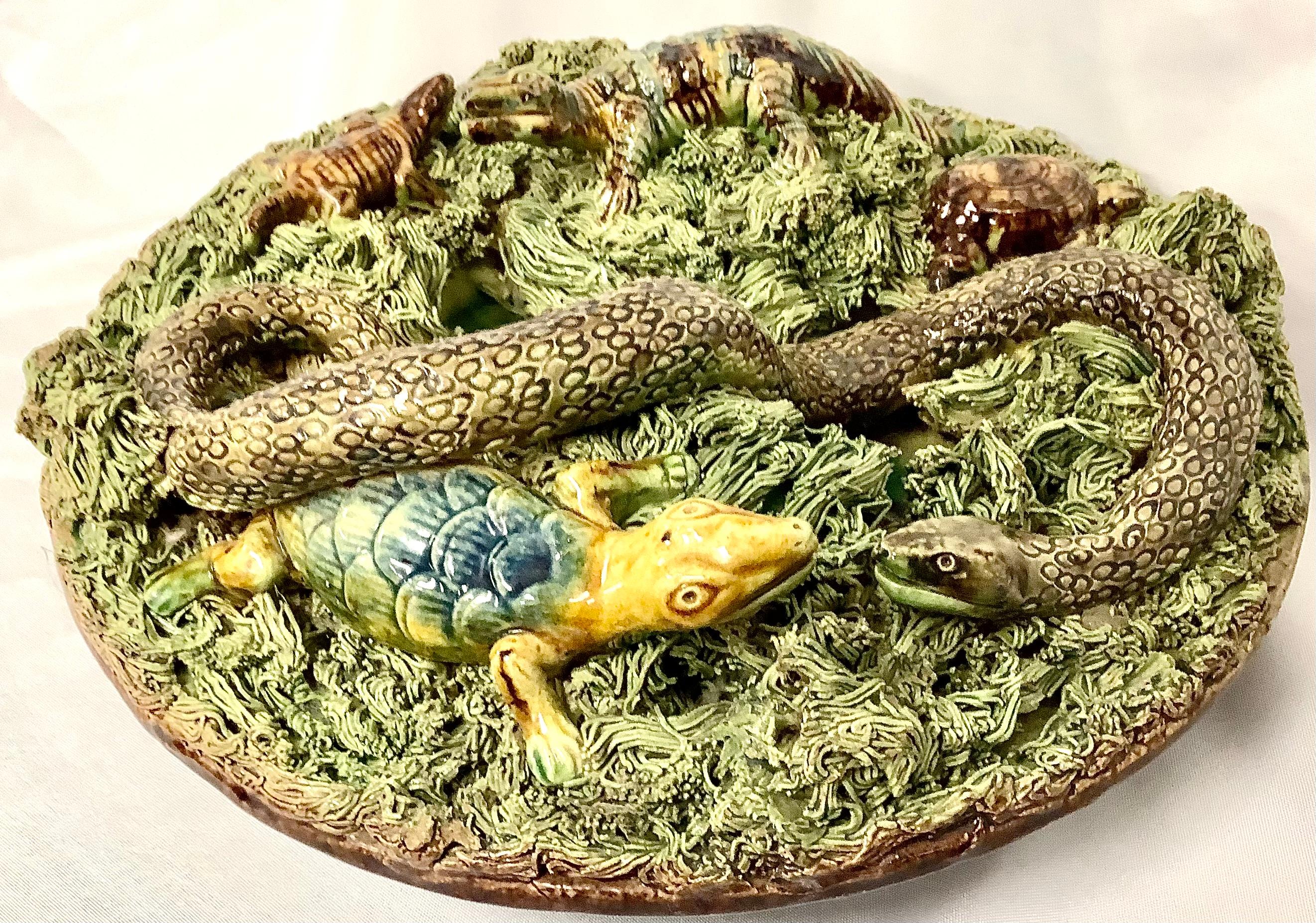 portugiesischer Palissy-Teller des 19. Jahrhunderts mit großer Schlange und mehreren Krokodilen, einer Schildkröte, die alle auf einem Moosbüschel nisten. Auf der Rückseite ist die große Nummer 6 eingeprägt. Die Farben sind Salbeigrün und Braun.