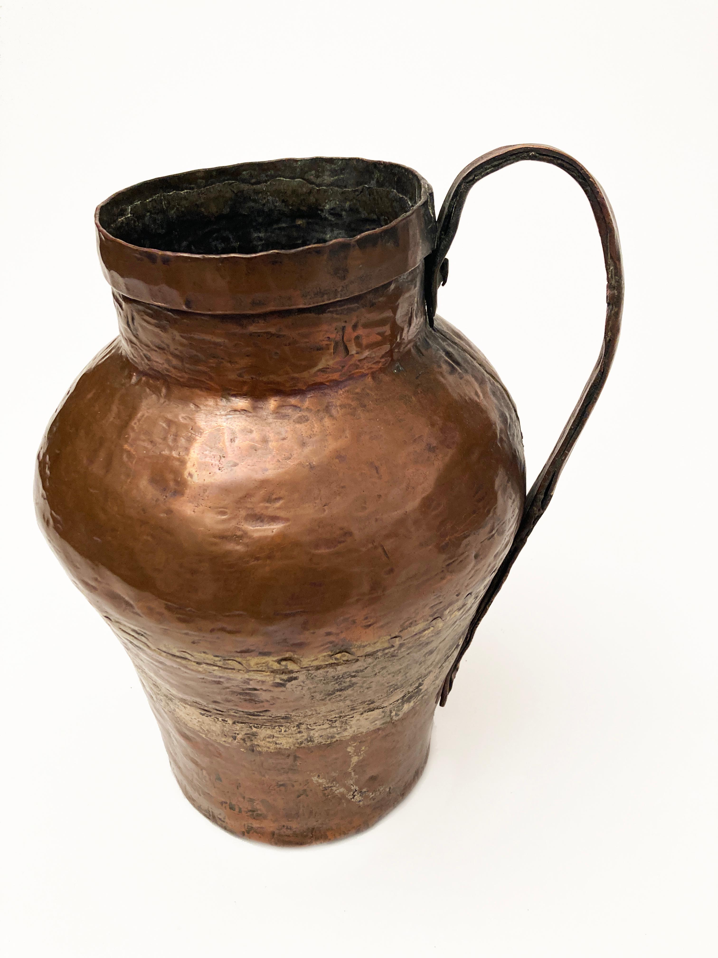 Copper vessels of this nature were once primitively made in Europe and Middle Eastern areas of the world. This piece is a stunning example of the stout, but primitive craftsmanship that went into creating it. This jug, most likely made for the