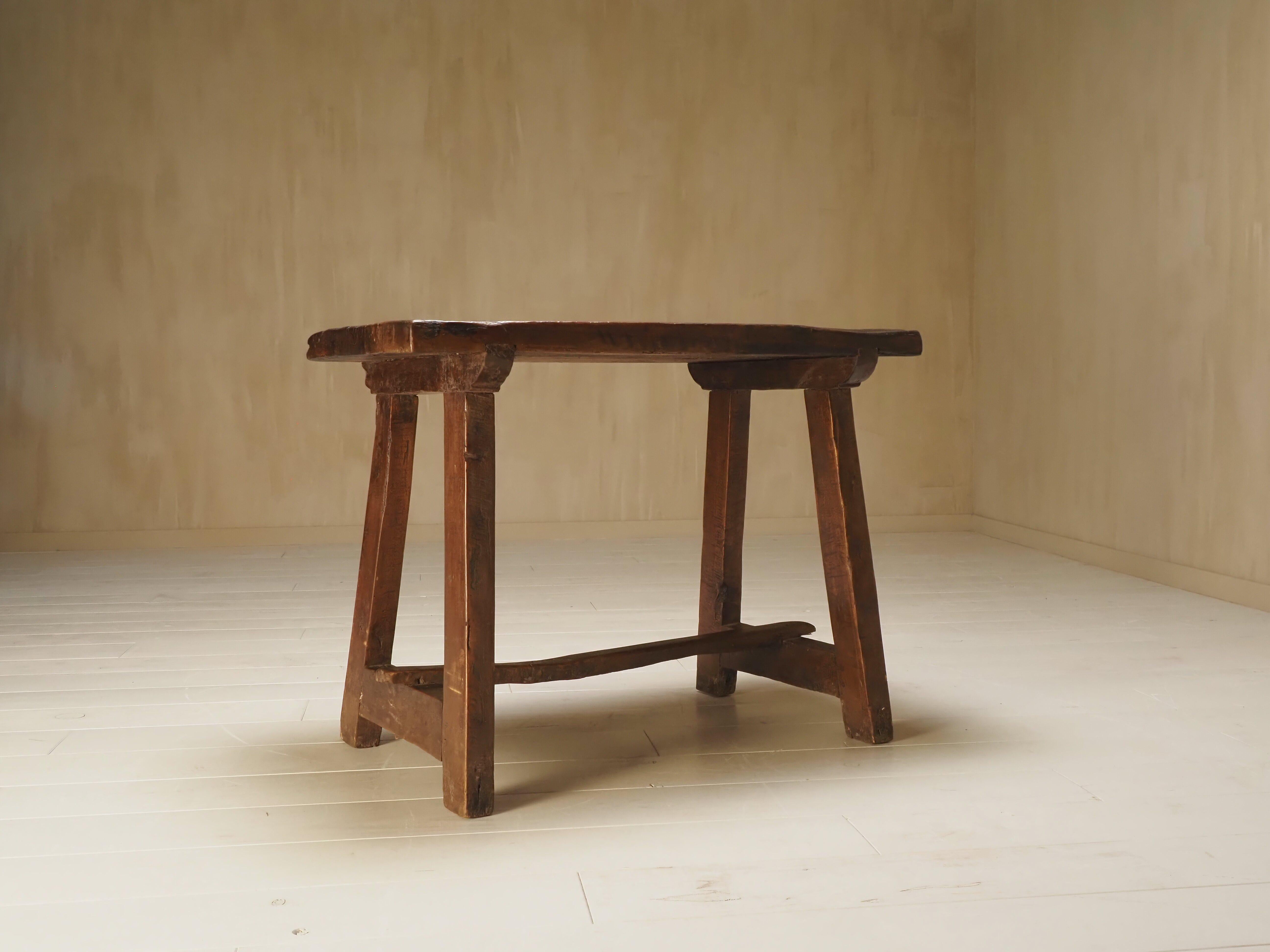 This unique piece is a rustic antique work table crafted from solid wood, dating back to the 19th century. Its raw, timeworn surface tells a story of centuries of use. The thick, uneven tabletop is marked by deep tool cuts, gouges, burnished patina,
