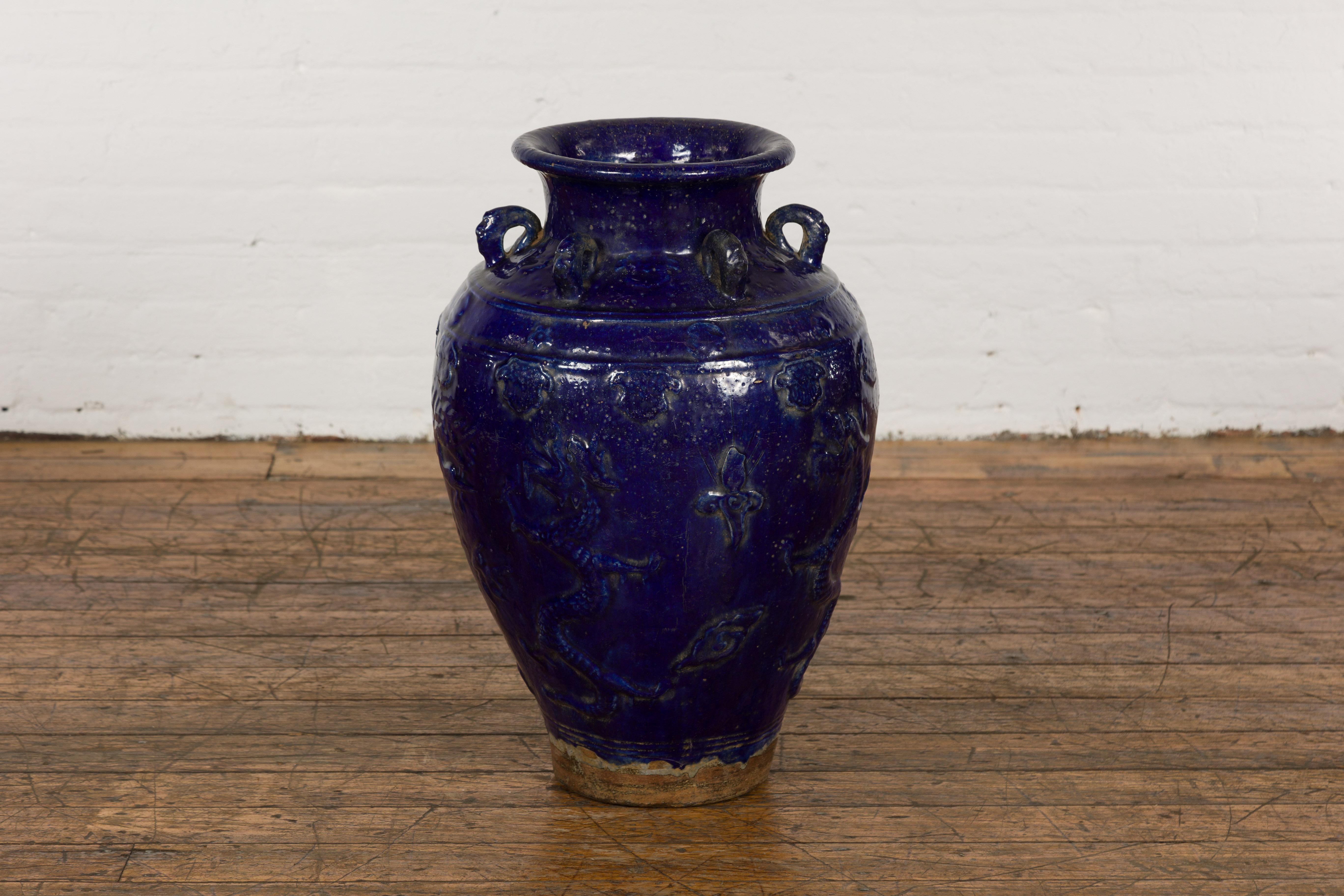 An antique Chinese Qing Dynasty period cobalt blue glazed Martaban jar from the 19th century with dragon, flower and cloud motifs, swan neck loops and unglazed bottom. Immerse yourself in the historic richness of Chinese art with this antique Qing