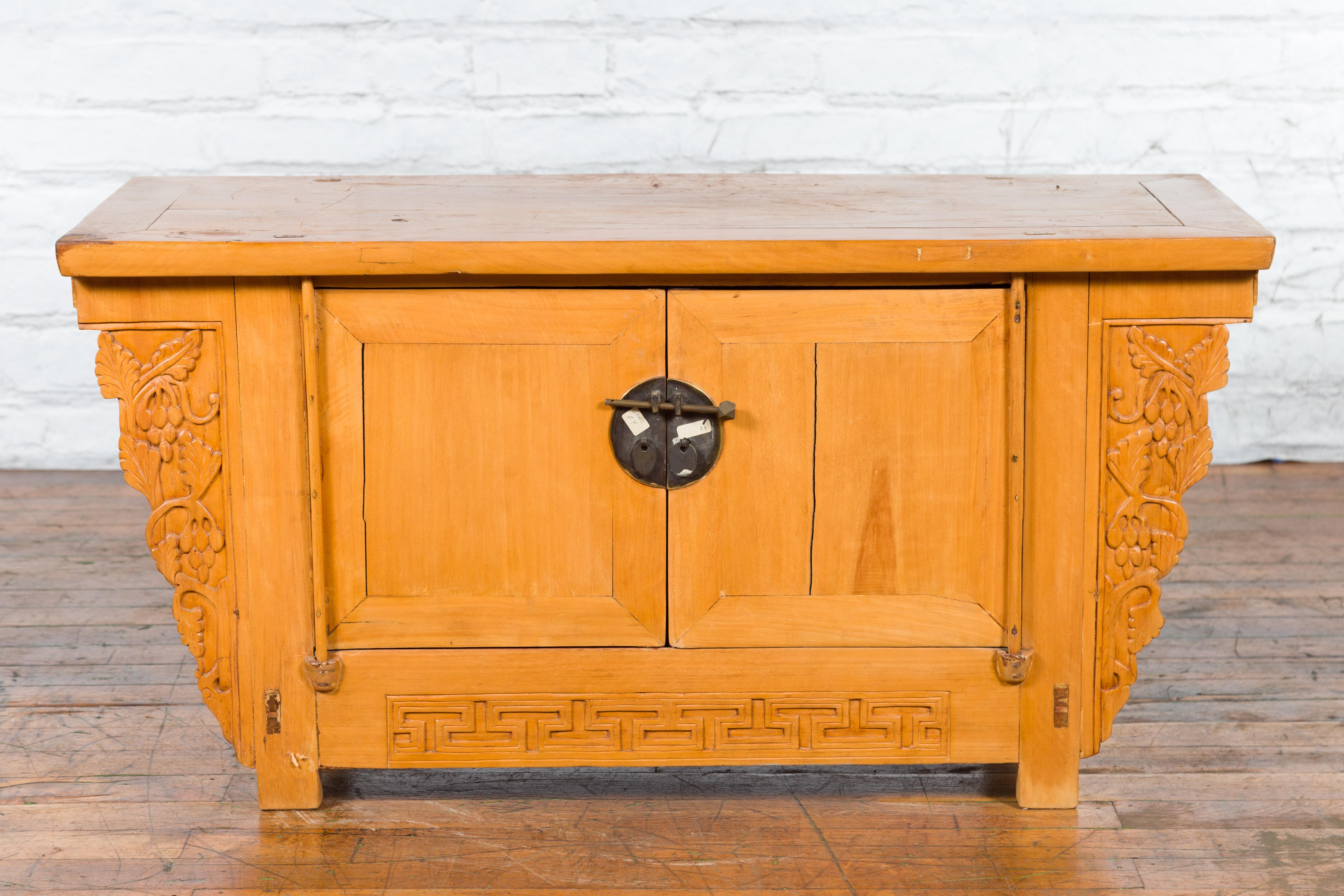 A Chinese Qing Dynasty period elm wood butterfly sideboard from the 19th century, with carved grapevines and meander motifs, natural finish and bronze hardware. Created in China during the Qing Dynasty in the 19th century, this elm wood sideboard
