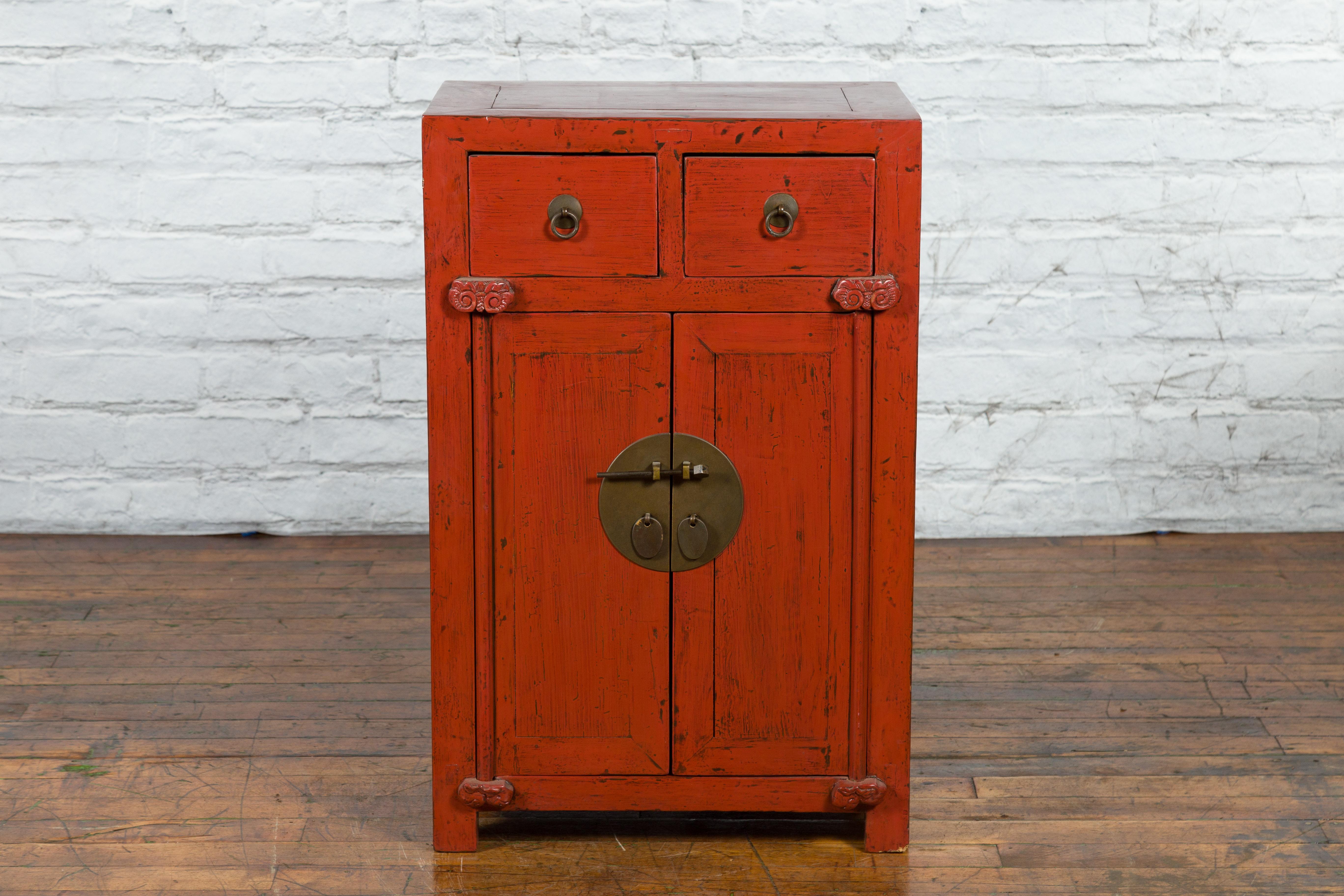 A Chinese Qing Dynasty period red lacquered cabinet from the 19th century, with two drawers, double doors, scrolling motifs and traces of black lacquer. Created in China during the Qing Dynasty in the 19th century, this red lacquer cabinet features