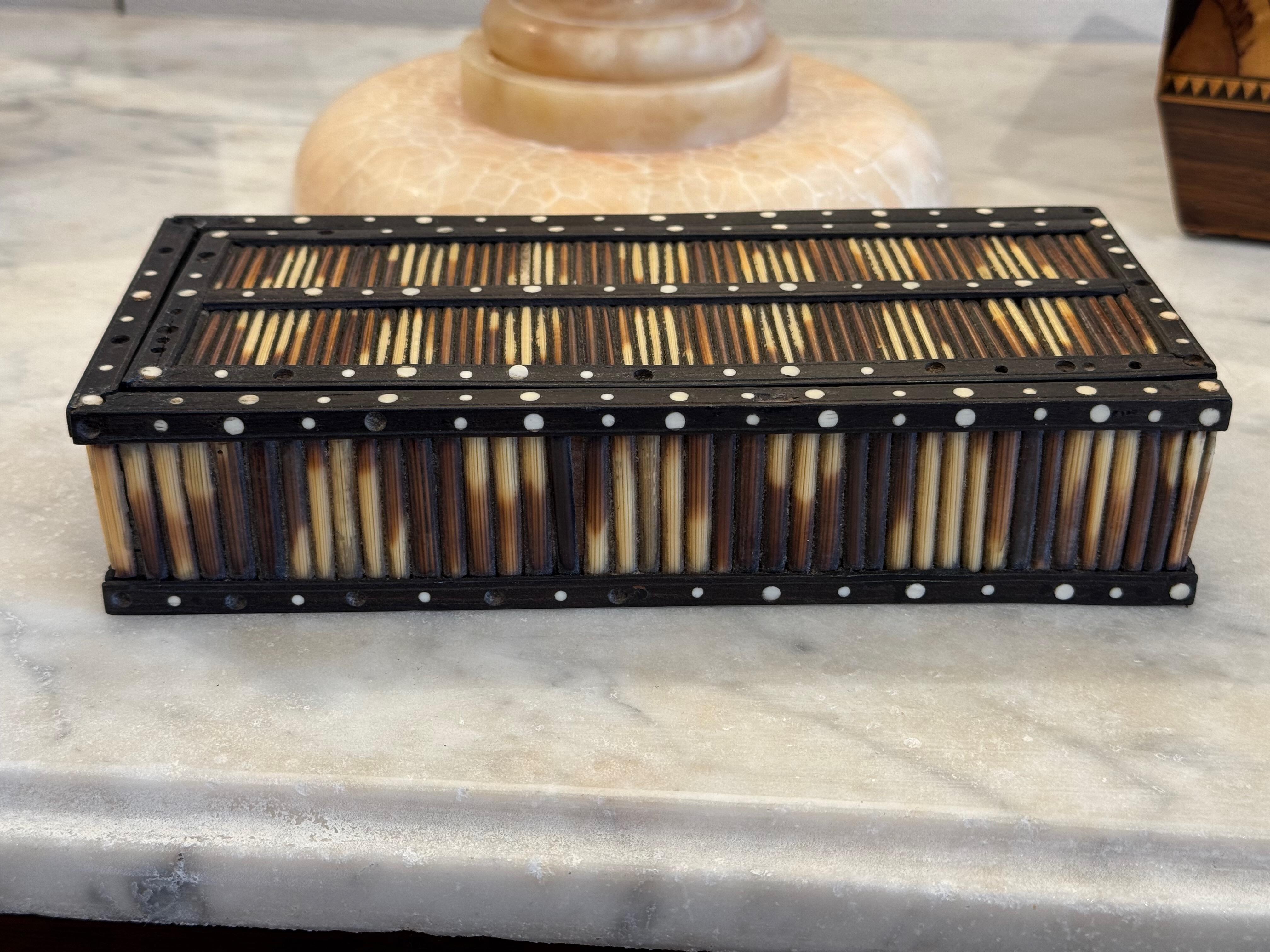 This 19th century decorative box features a sliding lid and is constructed with dark-stained wood, likely ebony, set with vertical porcupine quills around the body and lid. The edges are inlaid with contrasting white dots, lending a striking graphic