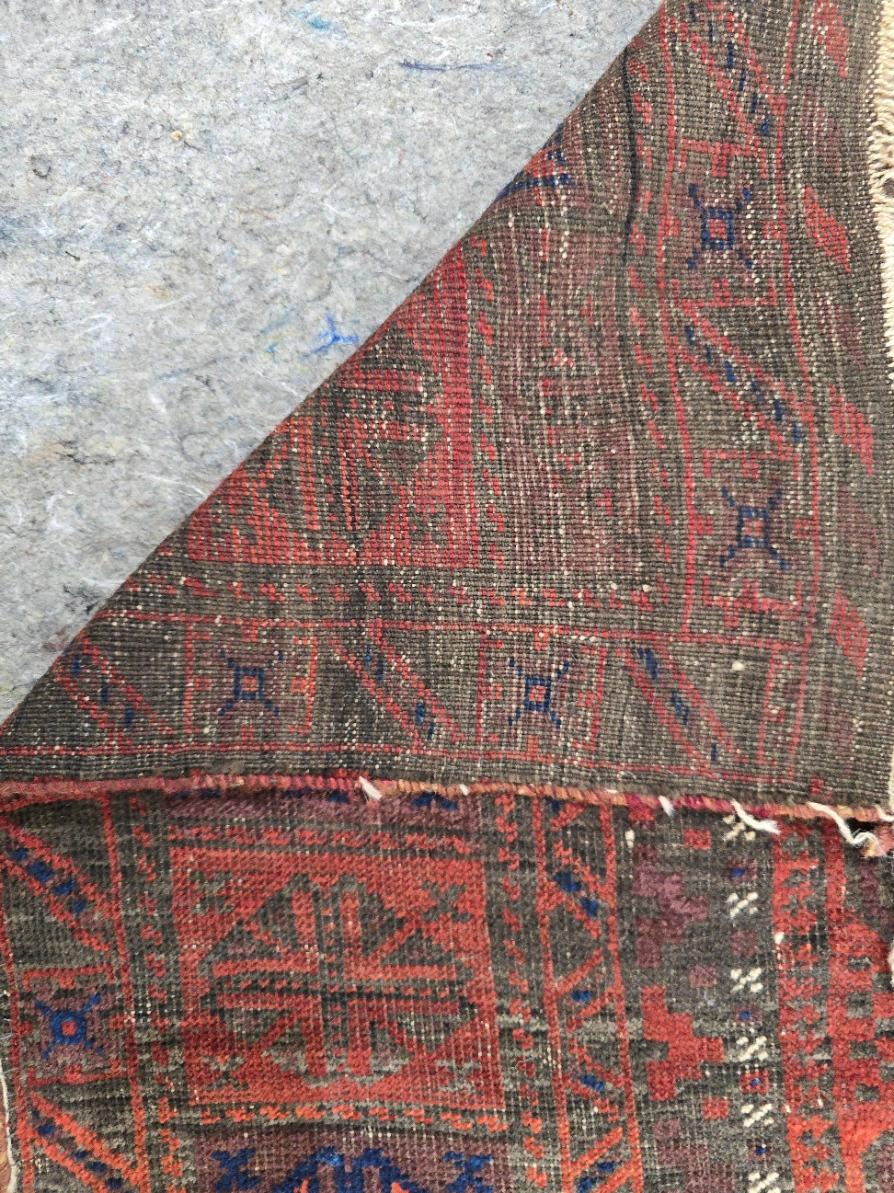 Embrace the rich heritage of tribal craftsmanship with this antique Persian Baluch rug, handwoven with intricate geometric patterns and earthy tones. Measuring 7.2 x 12.6 feet, this rug is a stunning example of nomadic weaving traditions, reflecting