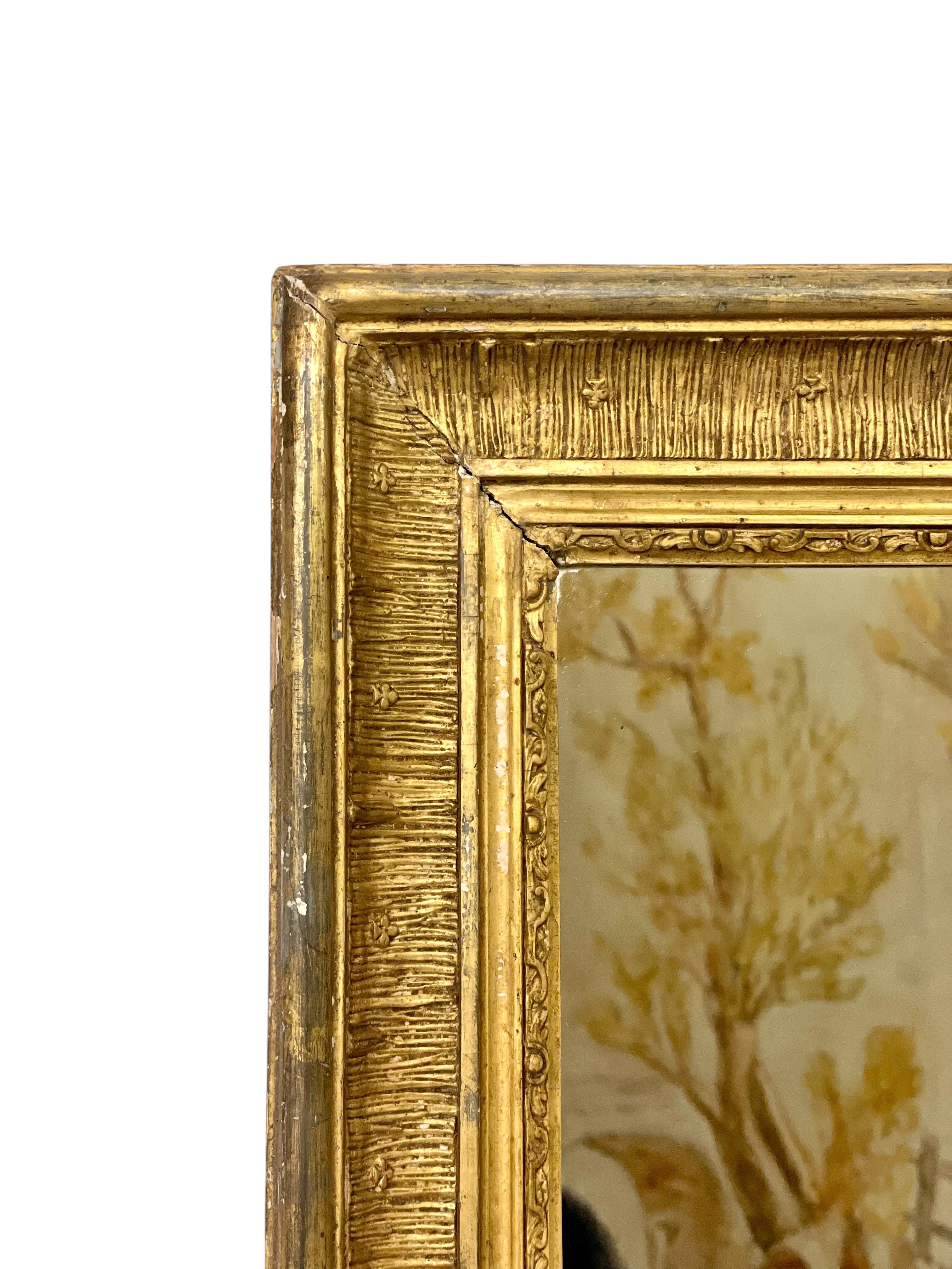 Este exquisito espejo de madera dorada del siglo XIX es un sorprendente ejemplo de fina artesanía y elegancia atemporal. El espejo está adornado con un marco de madera tallado a mano y ricamente detallado, recubierto de un cálido acabado en pan de