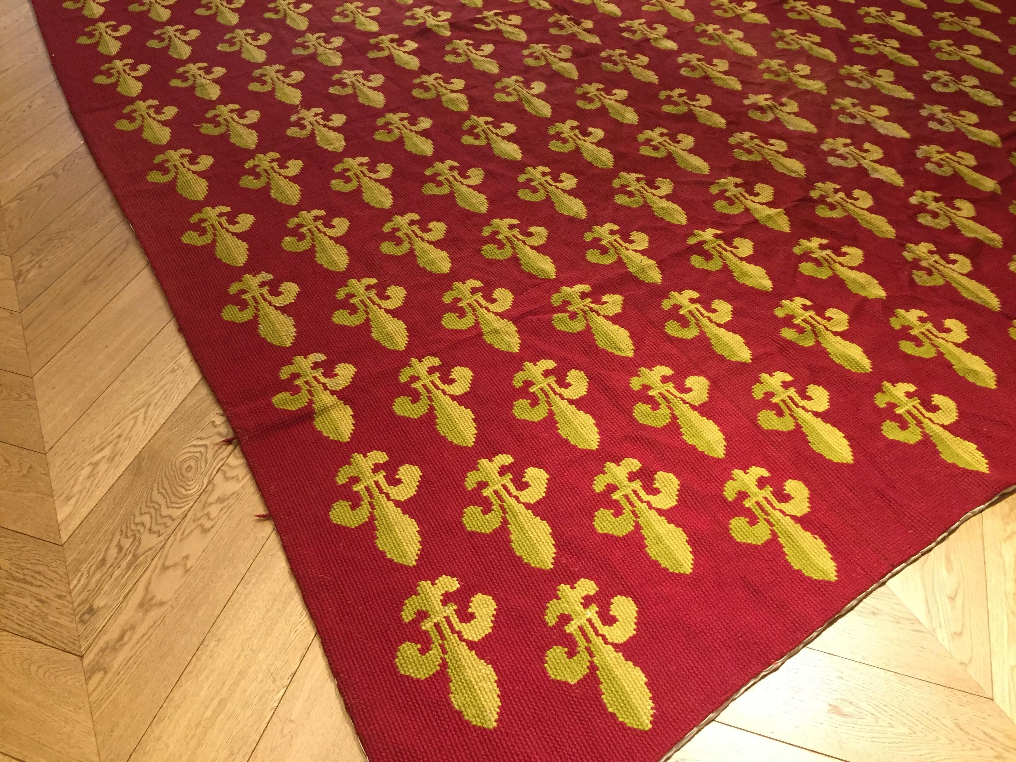 Large and antique carpet embroidered in thick wool with the heraldic motif of France's lily stands out in yellow and light green on a blood-red background. Usually, court ladies or convents were made these rugs on special events or important