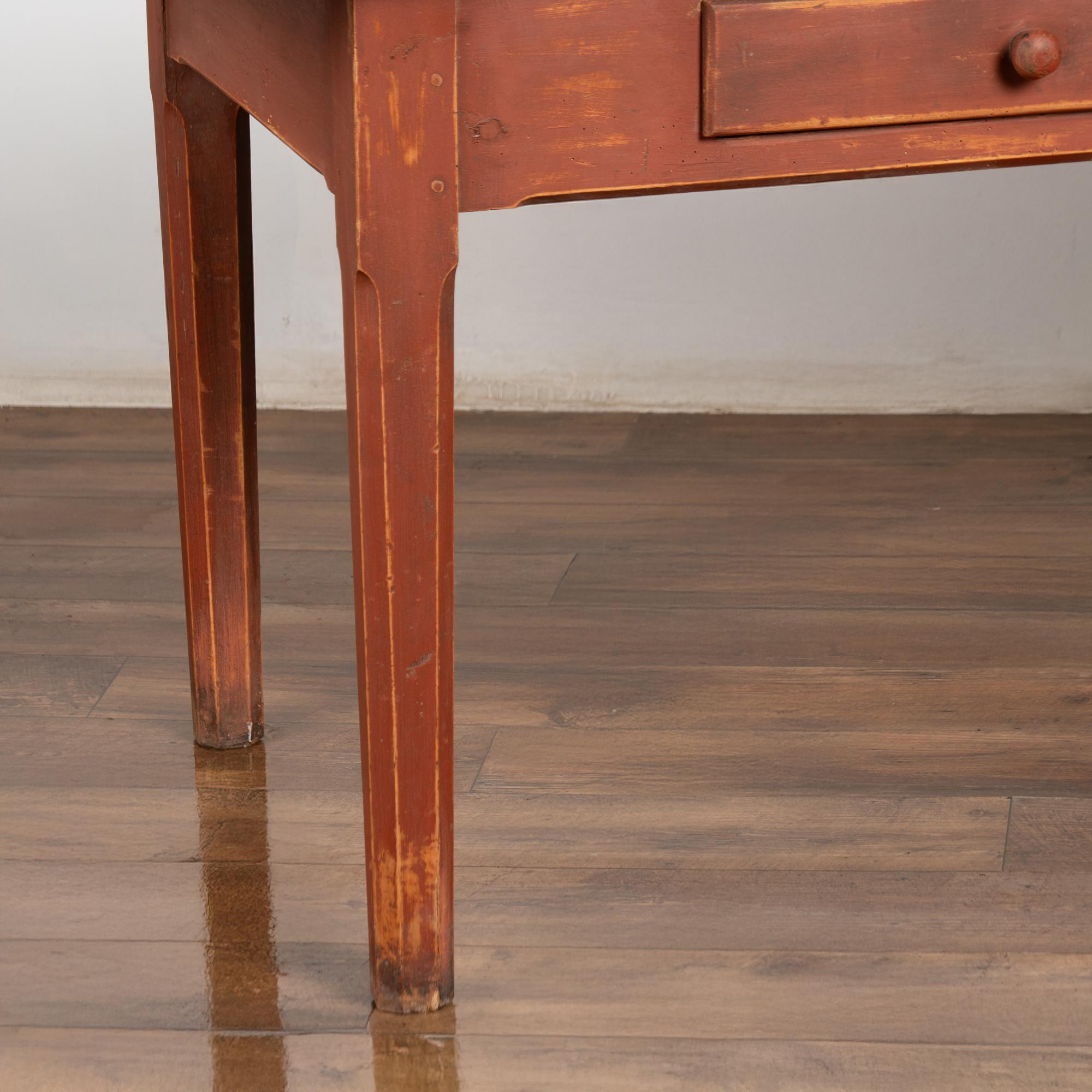 Table en pin suédois du 19e siècle avec finition peinte en rouge brique (plus tardive mais vieillie). Comprend trois tiroirs fonctionnels avec des boutons en bois et des clous en bois anciens visibles.
Le dessus présente des signes d'usure dus à