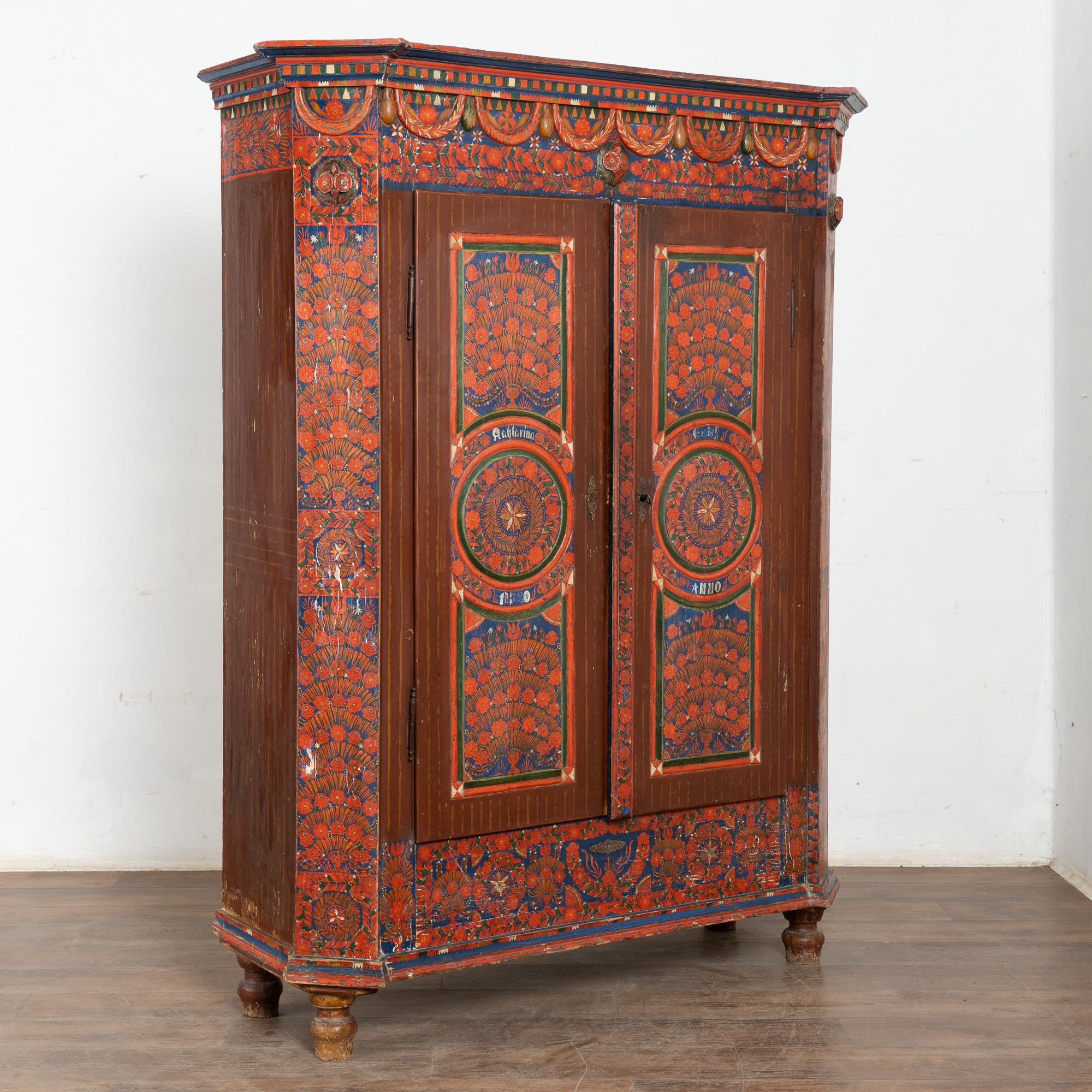 This painted pine armoire still maintains the quality and details of the elaborate hand-painted finish. The vibrant red and blue patterns were traditional Eastern European folk art style elements of the era. The many carved details elevate this