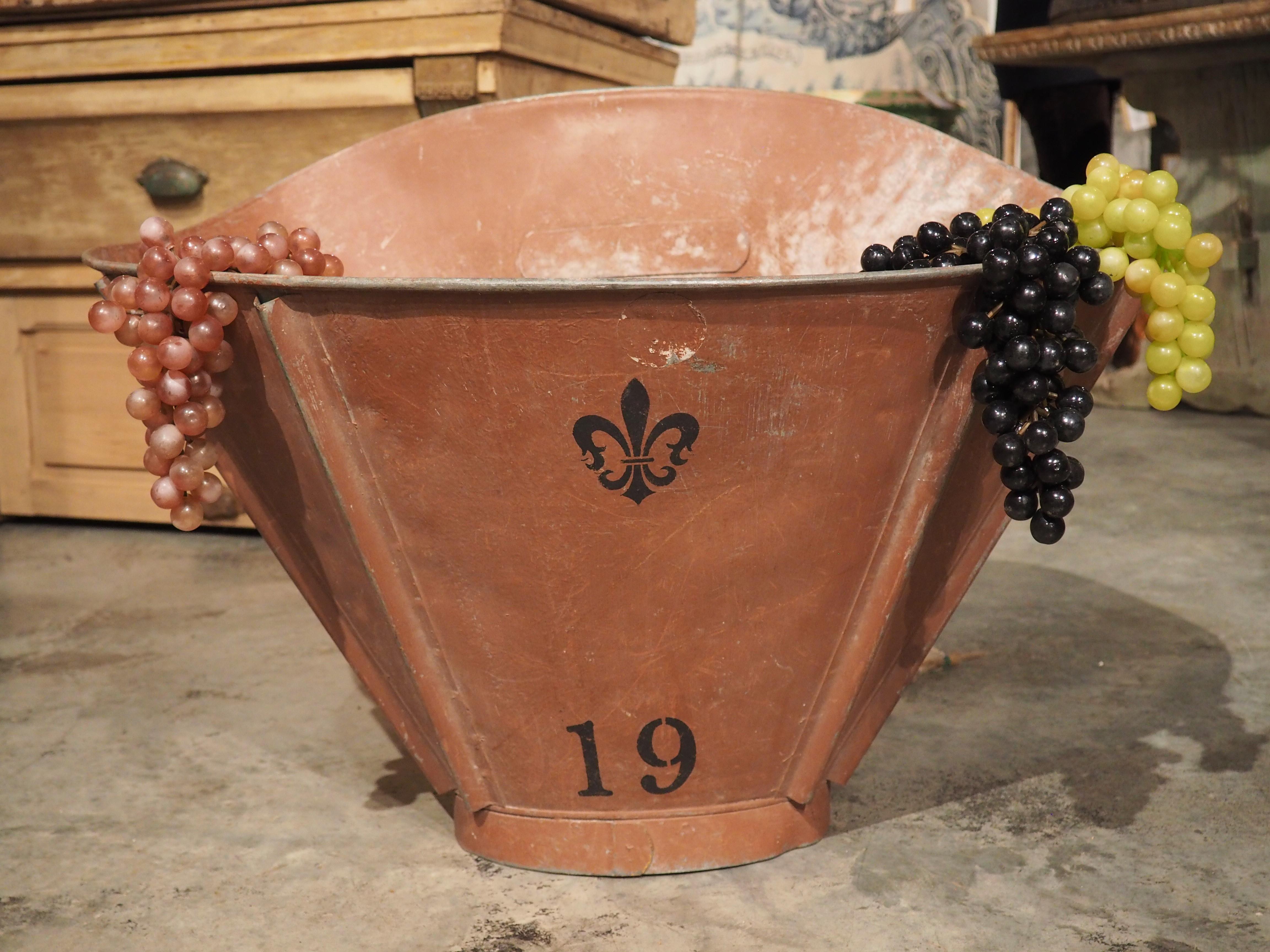 A large red hotte, with a black painted fleur de lys and the number “19”, this grape harvesting basket would have been used in Burgundy, France, during the 1800’s. The original canvas straps are still affixed to metal hooks on the back, which would