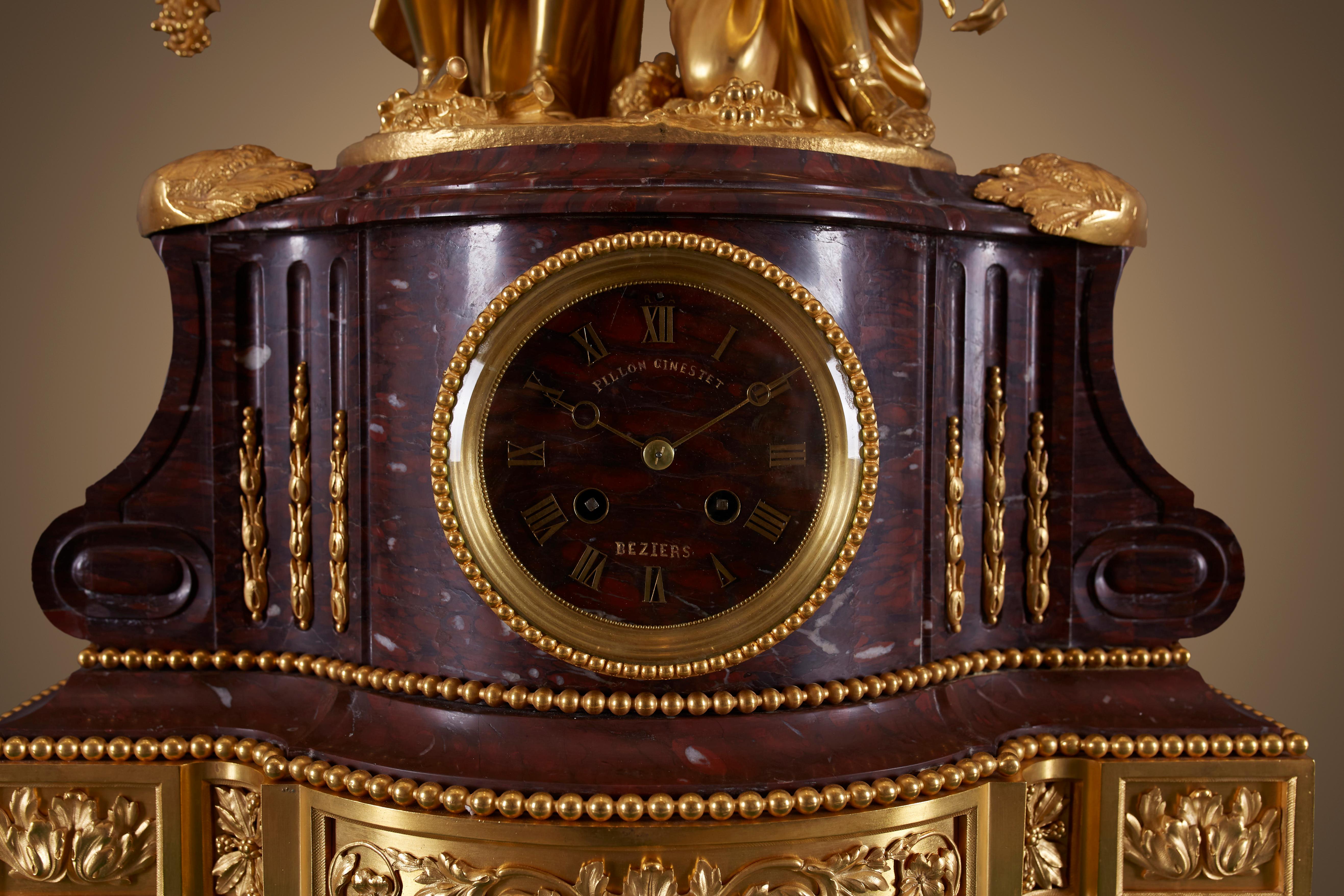 A mantel clock crafted from gilt and gilded brass (also known as ormolu) and red griotte marble in the eclectic style popular during the Napoleon III period.

The mantel clock features a central griotte marble pedestal clock case with a circular