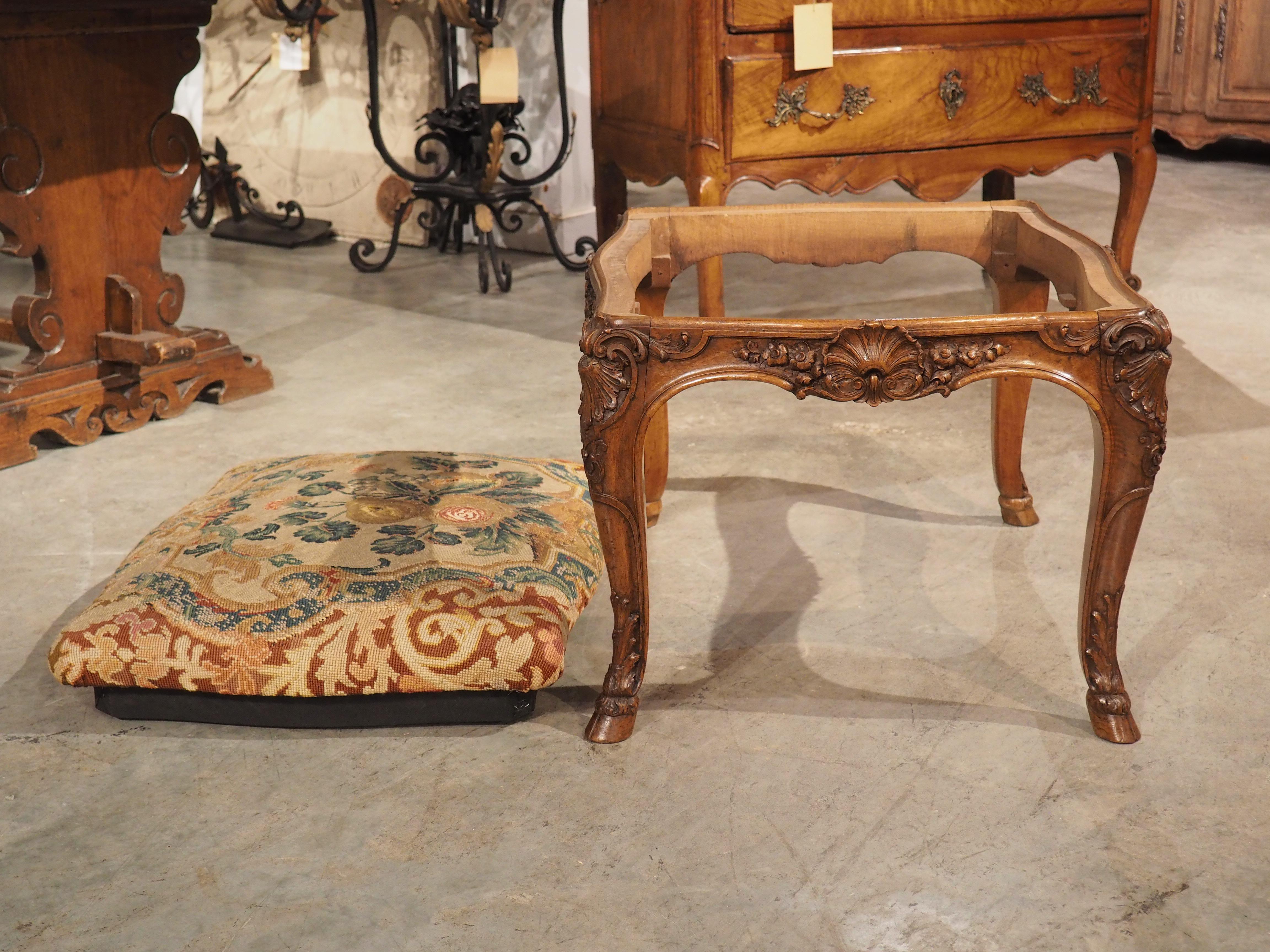 Dieser Tabouret im Regence-Stil wurde um 1800 in Frankreich aus reichem Nussbaumholz handgeschnitzt und trägt unter dem Sitz einen Produktionsstempel mit der Aufschrift 