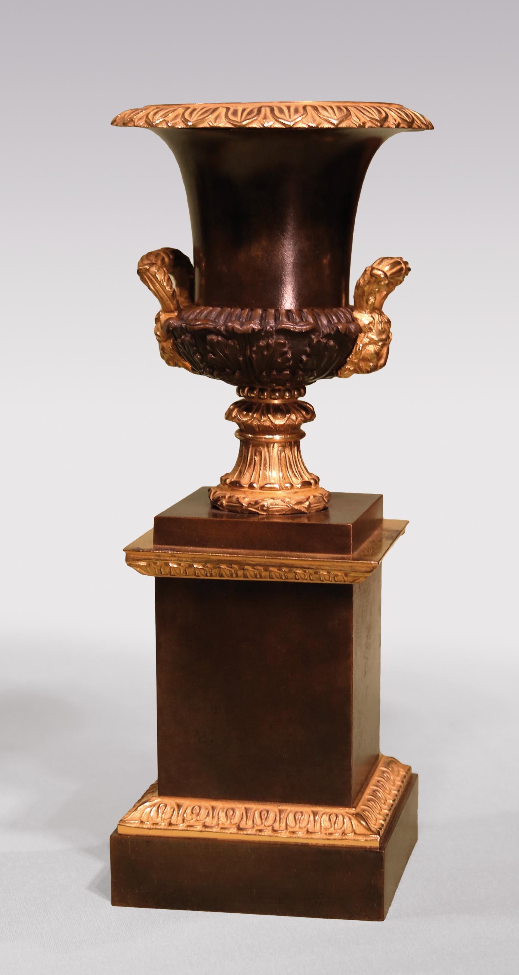 A pair of early 19th century Regency period bronze and ormolu campana shaped Urns, having leaf moulded rims above acanthus leaf decoration with lion's head handles, supported on plinth bases.