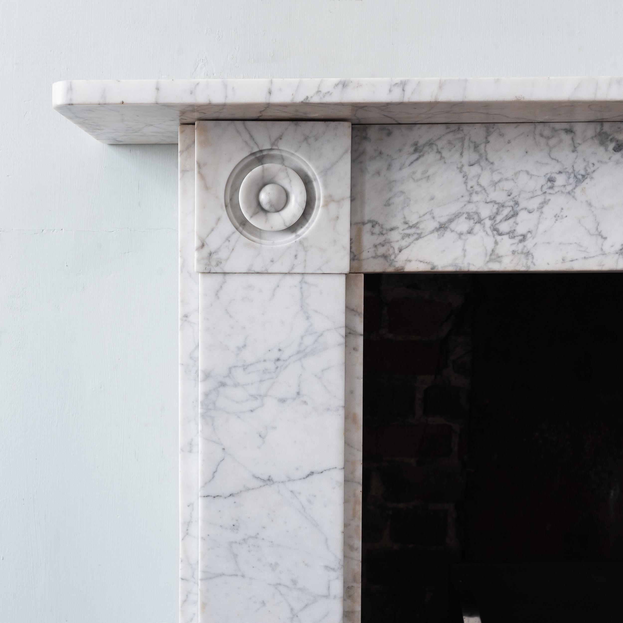 Nineteenth century English Regency period Carrara marble roundel fireplace, of simple plain form with deep-undercut bull's-eye corner-blocks.

Opening width 80 cm x 91 cm height, Outside jamb to jamb width 115 cm.

Ready for installation and use.