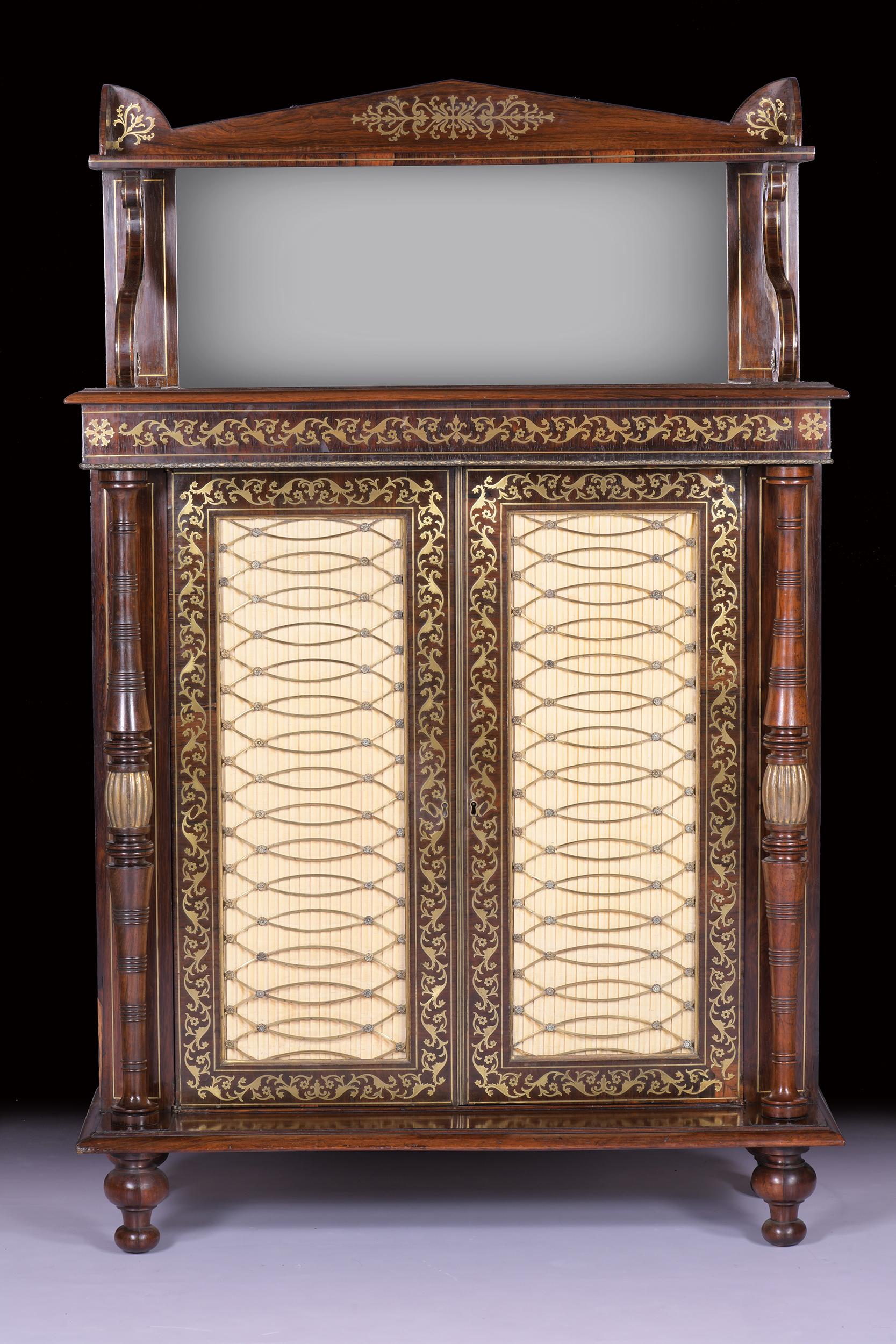 A Regency brass inlaid chiffonier inlaid with scrolling foliage and rosettes, the triangular pediment and conforming galleried shelf above a mirror inset panel, on S-scroll supports, over a pair of pleated material and interlacing brass grill inset