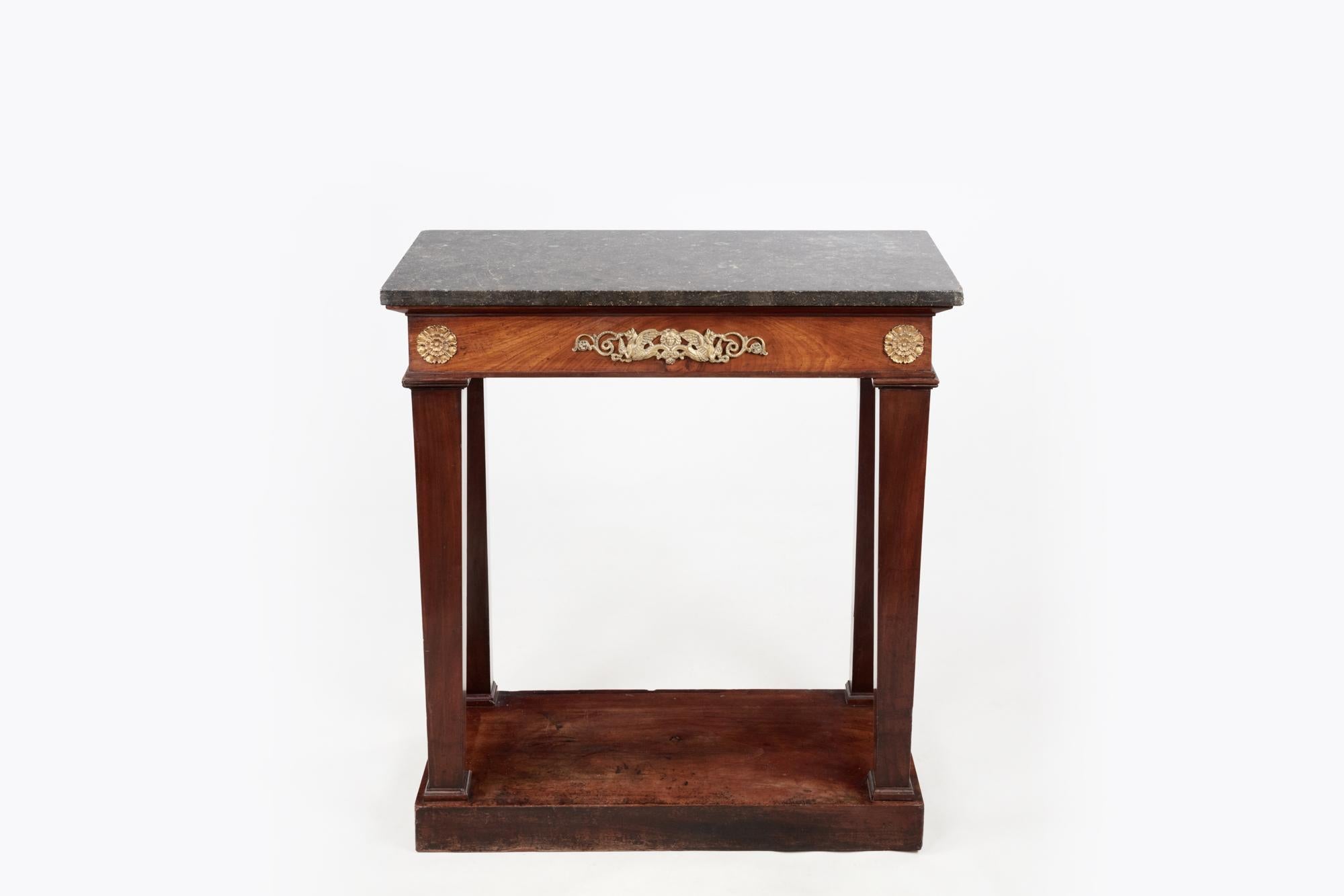 A simple yet elegant Regency-era console table is a fine example of period design. Featuring a black marble top, which is set above the mahogany frame of the table. The apron is mounted on either side with gilt bronze rosettes and set to the centre