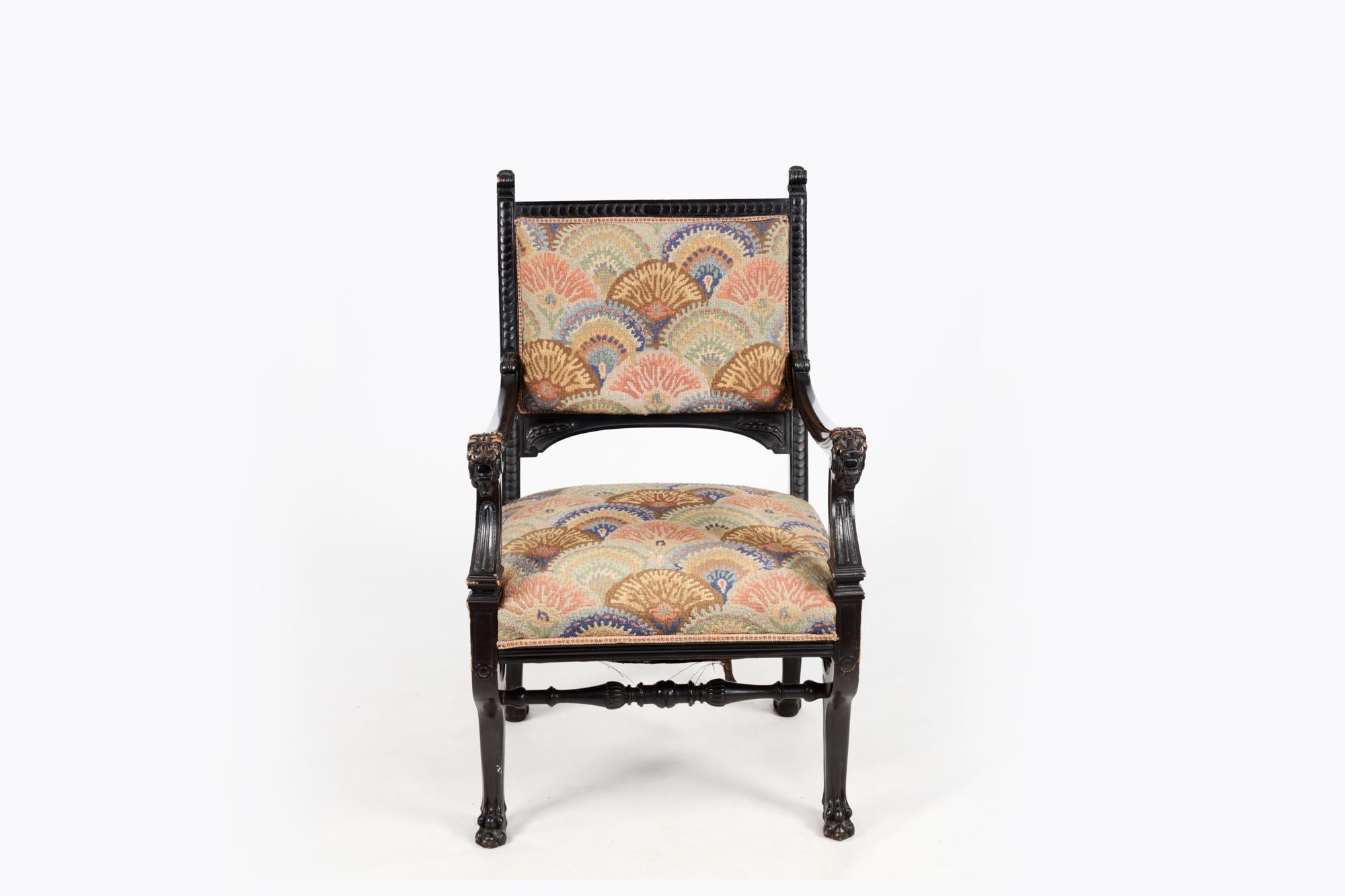 19th Century Regency ebonised carved library chair with needlepoint back and seat, of solid wood construction and finely carved details. The arms of the chair terminate in carved lion masks and the legs terminate in four hairy paw feet. It features