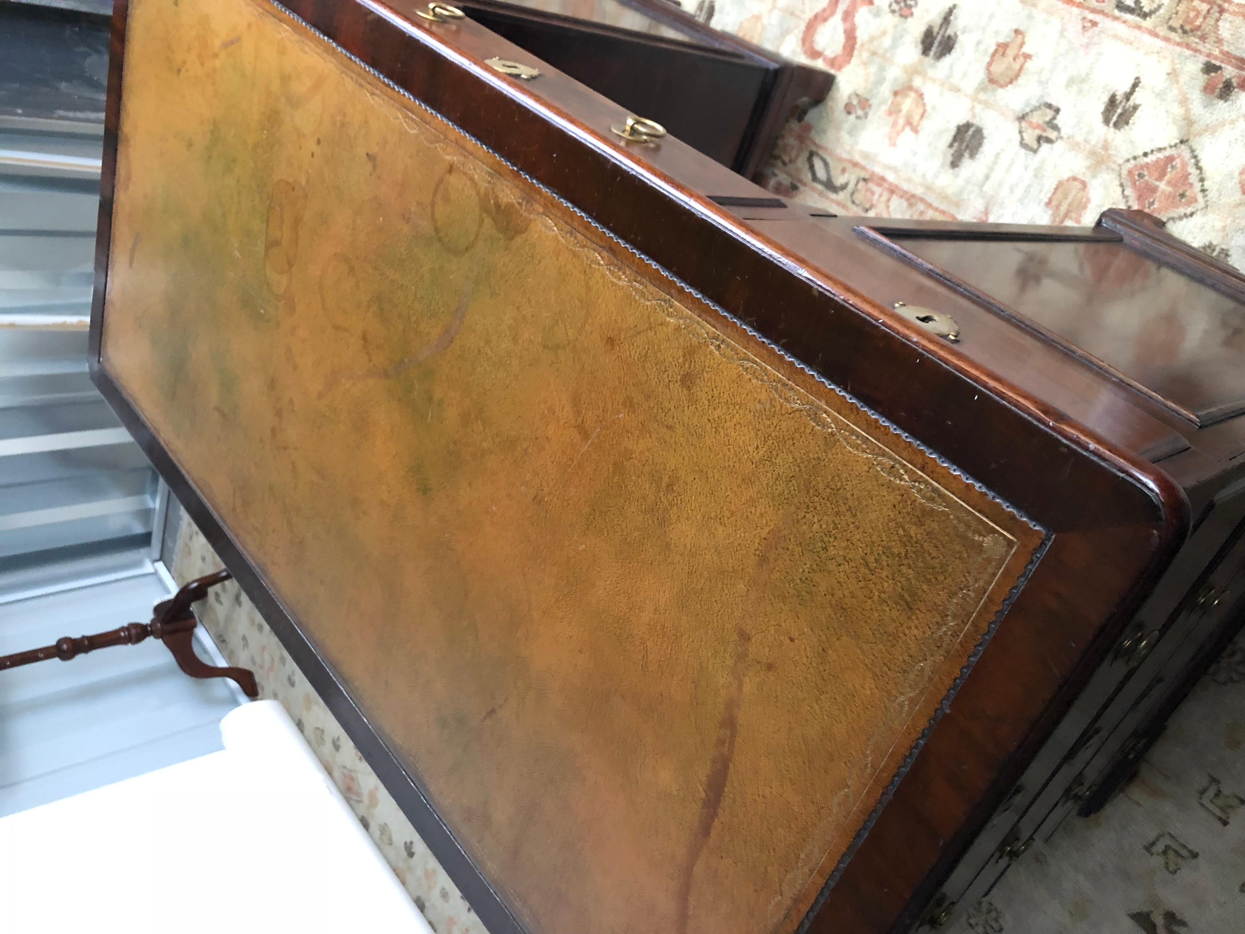 19th century English kneehole desk of mahogany created in the Regency style. The writing surface has an inset camel leather embossed top. The front of the case contains three drawers over a kneehole opening and cabinet door, flanked by paneled