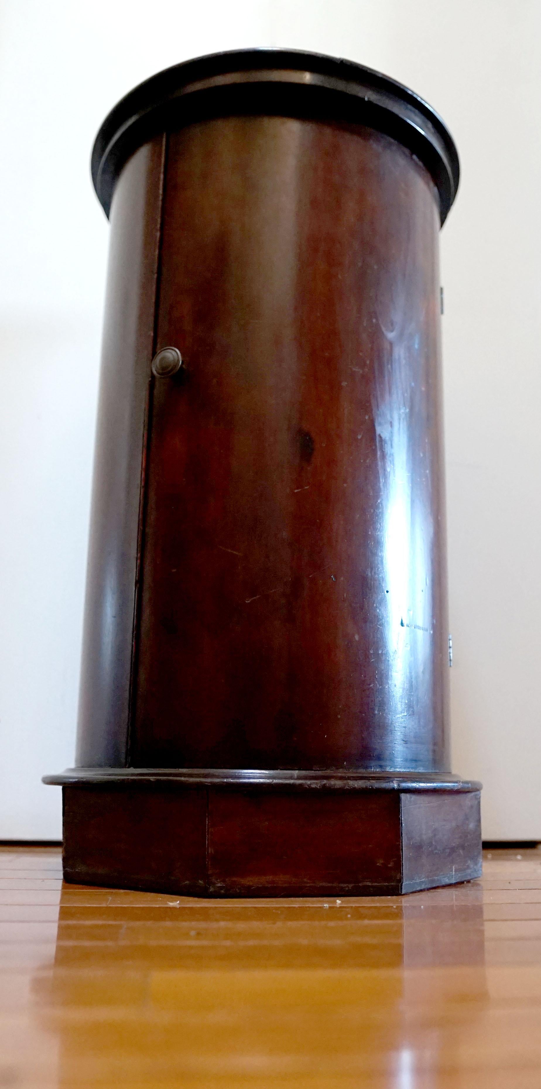 Der zylinderförmige Schrank ist mit weiß und grau geädertem Marmor verkleidet. Der Regency-Mahagonischrank wurde im zweiten Viertel des 19. Jahrhunderts in England hergestellt. 
Der kreisförmig geformte Rand umschließt eine Platte aus weißem