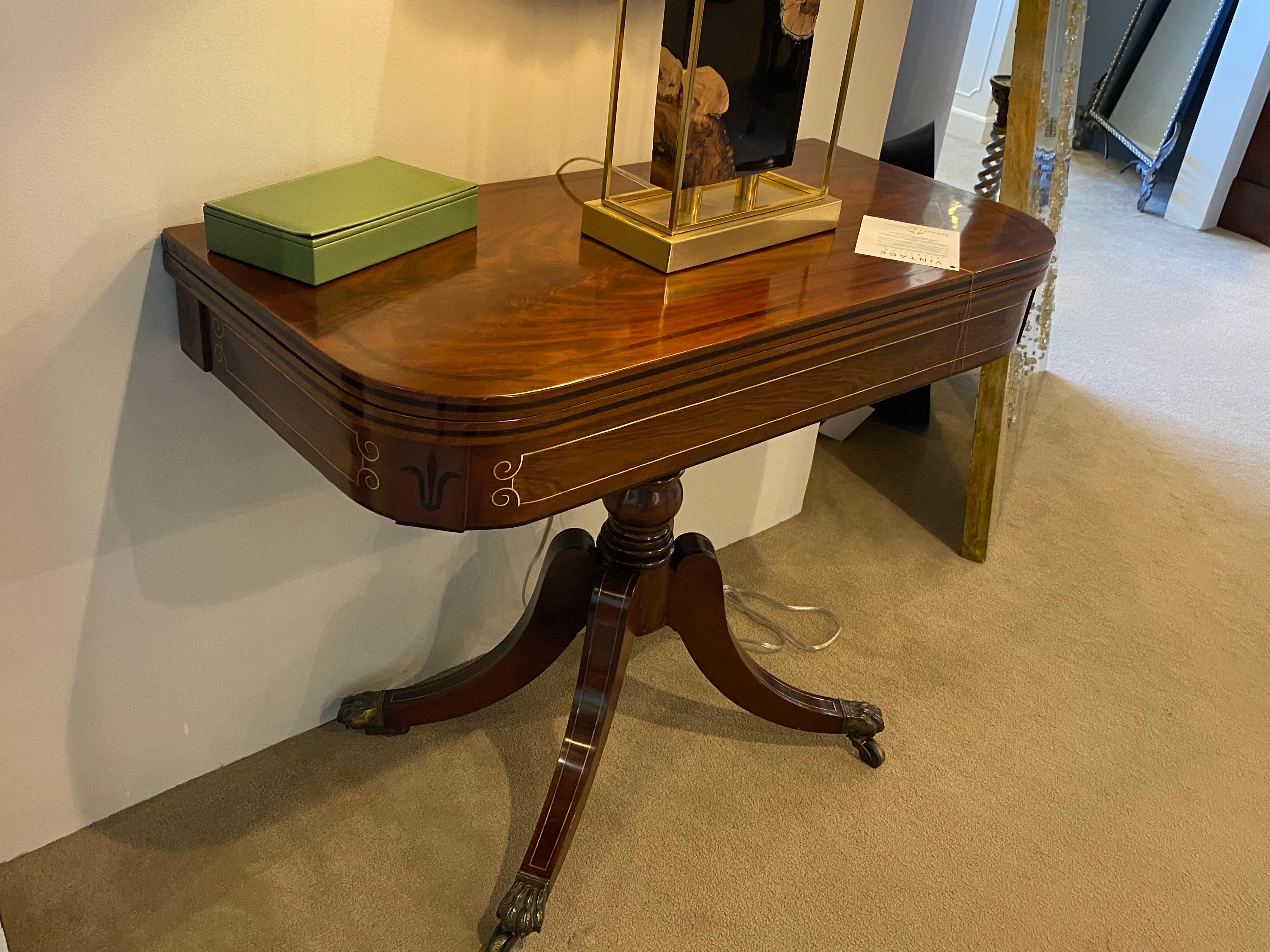 A lovely grained 19th century mahogany and rosewood games table with brass inlay on the apron and the legs. Solid brass toe caps and casters. This fold over games table is an excellent piece as a console in an entrance or hall. It has good color and