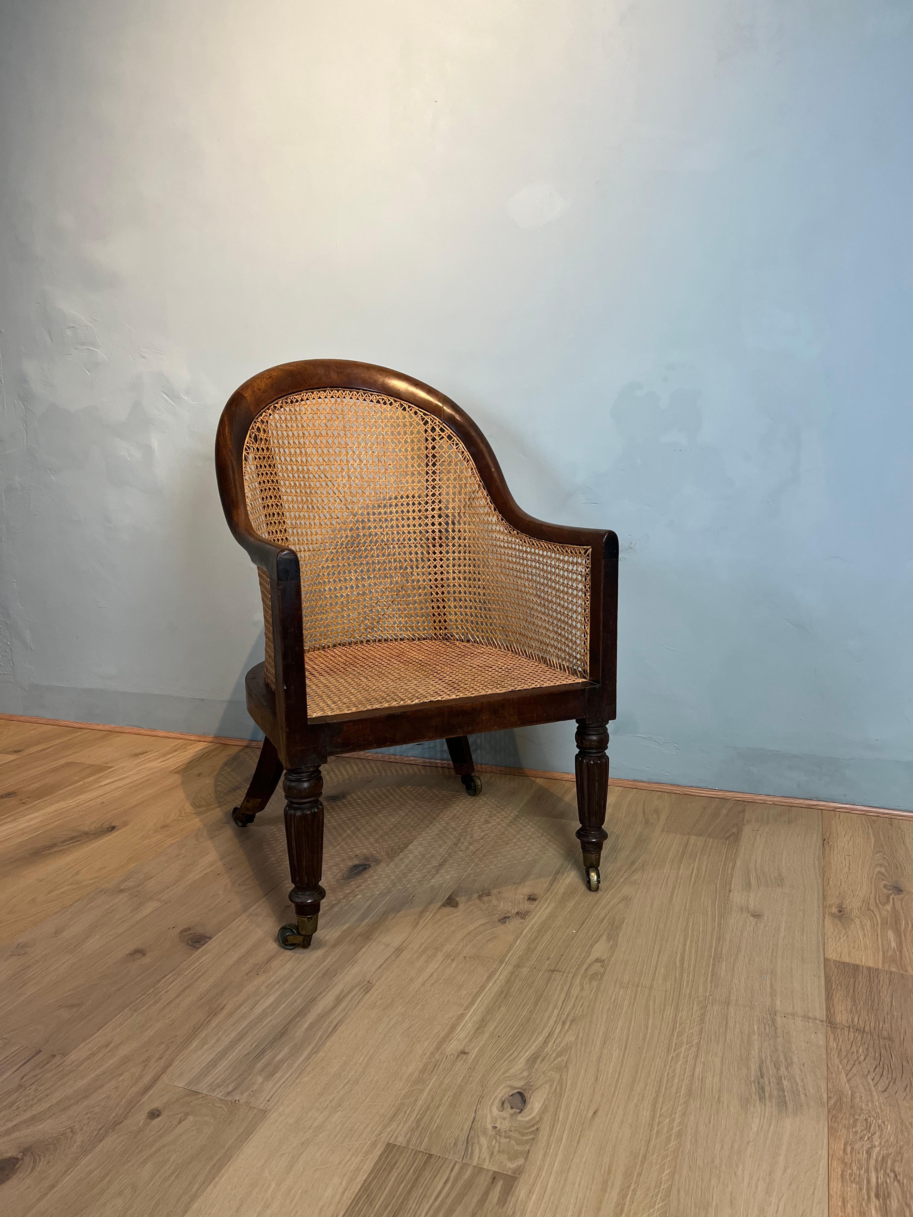 This Regency mahogany Bergere arm chair has a delightful flowing shape to the cresting rail and back legs with elegant classic reeded turned front legs, finishing on brass casters. The traditional caning is in excellent condition and the mahogany