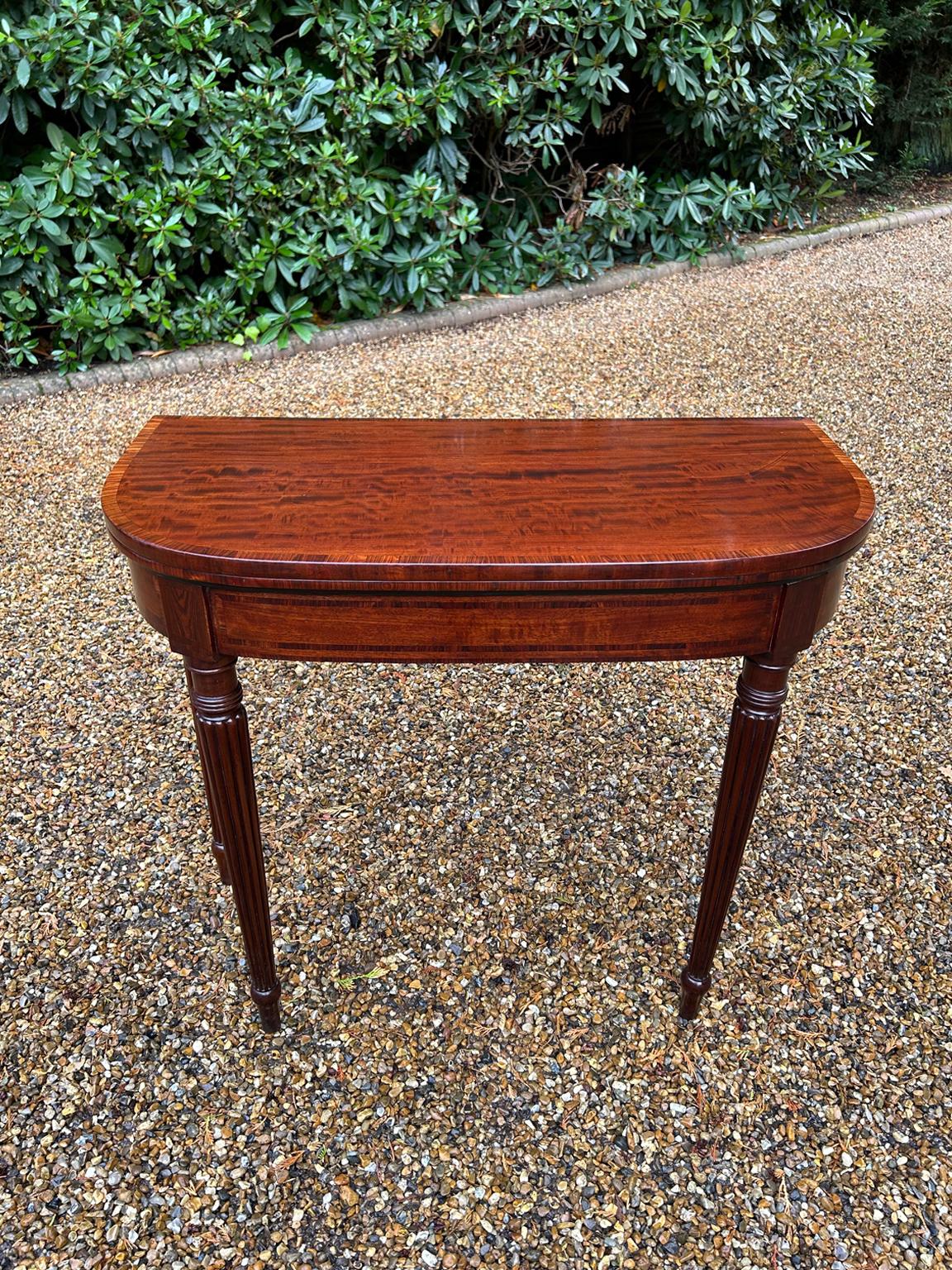 Table à cartes en forme de D en acajou de style Régence avec incrustation et bandeau en bois de rose sur des pieds fuselés tournés et cannelés. Les deux pieds arrière pivotent, le plateau s'ouvre pour devenir une table à cartes avec un intérieur en