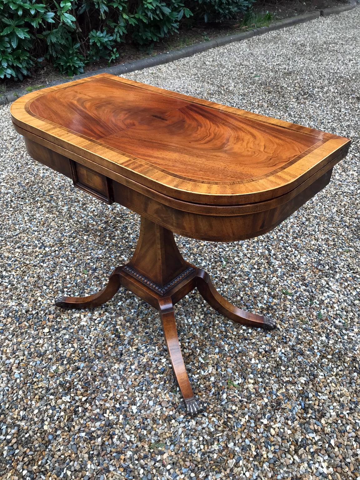 An original 19th century Regency inlaid crossbanded D-shaped mahogany card table with baize interior. Raised on a tempered chamfered column and splayed leg supports ending with brass claw feet and castors. The top swivels open to become a card